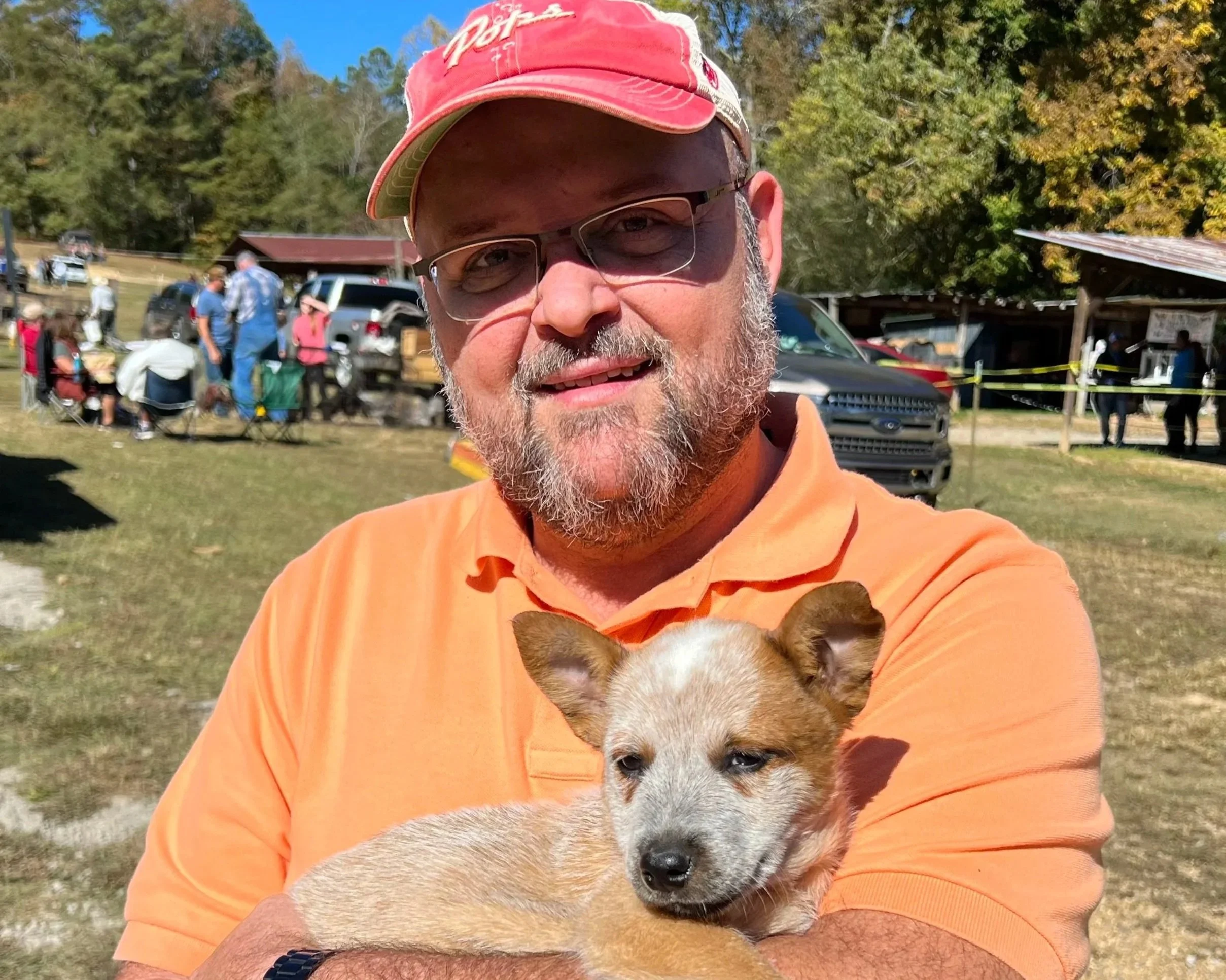 A man with glasses, a bald head, and a goatee, wearing a suit and tie, smiling in front of an abstract red and orange background.