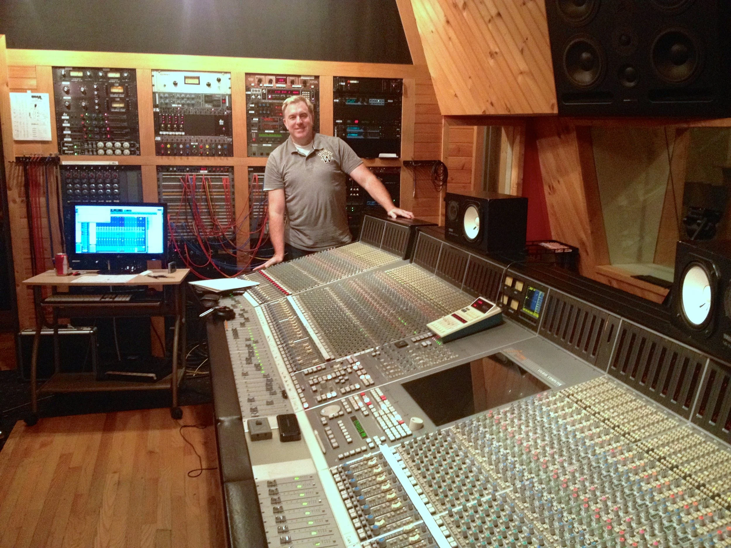 Shane Adams standing at a large studio mixing console