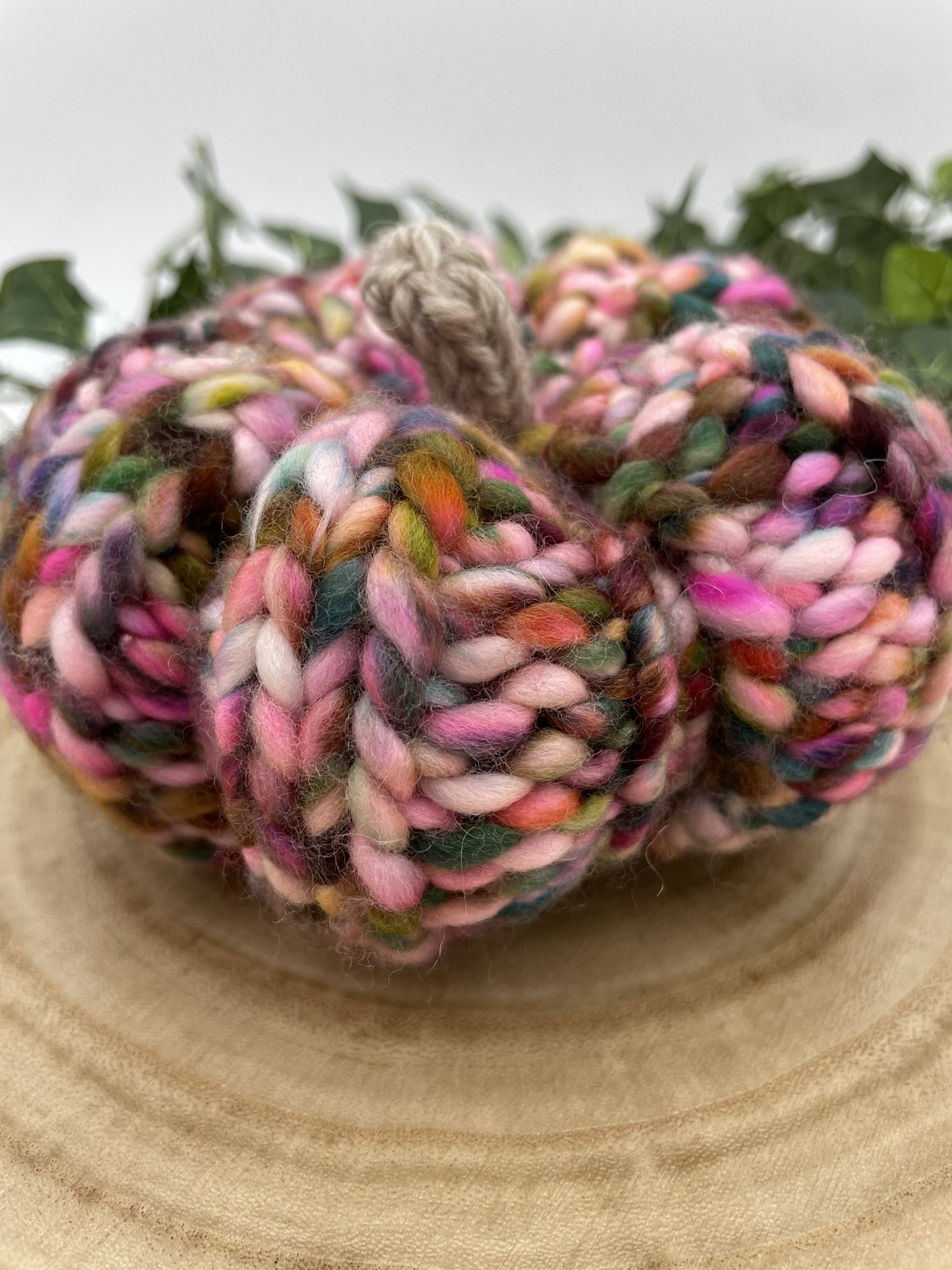 Angled view of a hand-knit pumpkin in fall colors with multicolored yarn and beige stem.