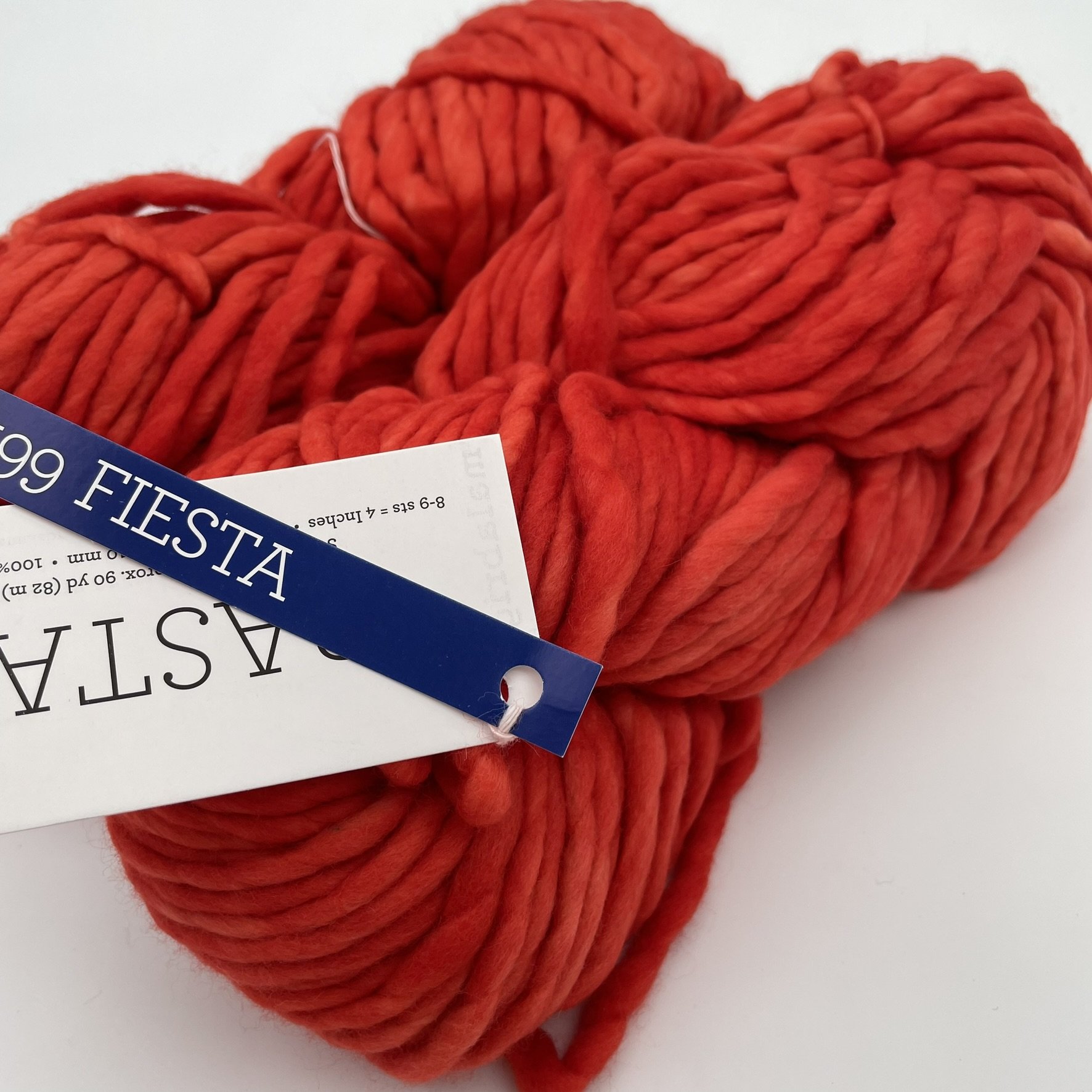 Close-up of Malabrigo Rasta yarn in Fiesta colorway, showcasing vibrant red-orange shades in super bulky merino wool.