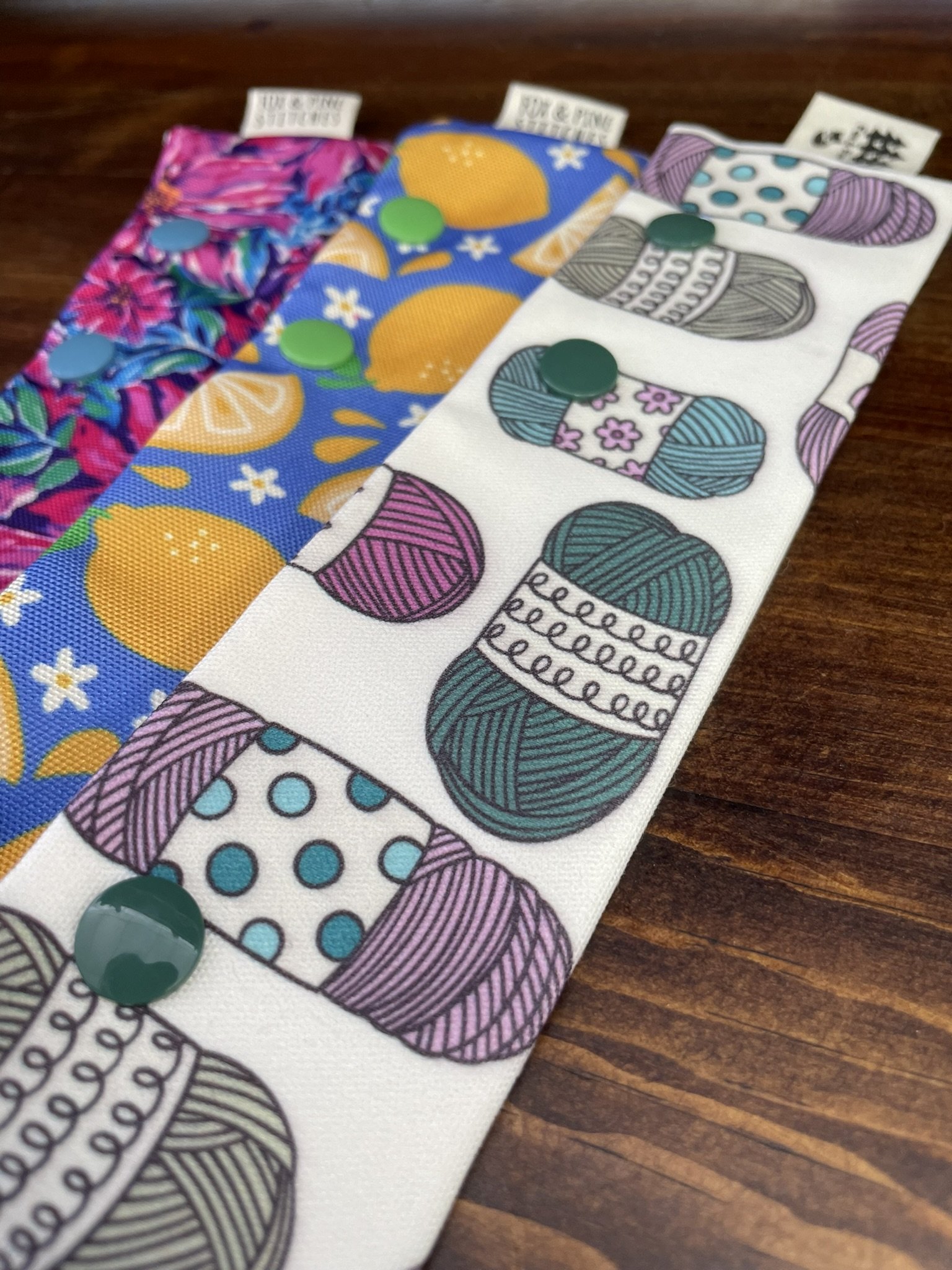 Fox & Pine double-pointed needle holders in floral, lemon, and yarn designs displayed at an angle on a wooden surface.