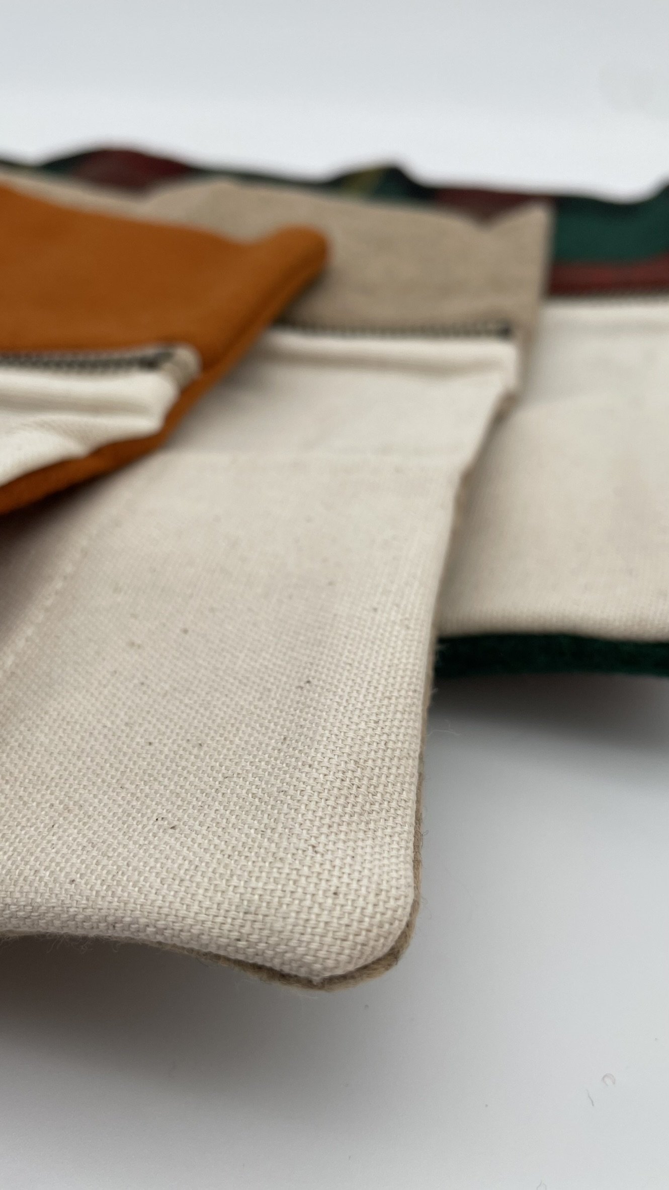 Close-up corner view of stacked Twig & Horn wool knitting tool pouches in orange, natural, and plaid designs, highlighting the textured wool fabric.
