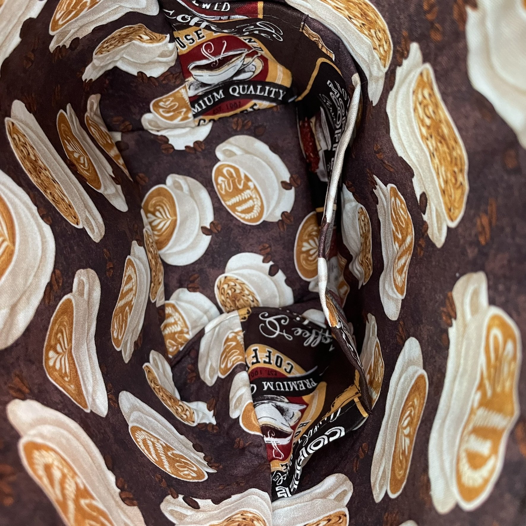 Interior view of a large coffee-themed project bag, showing deep pockets for yarn storage and accessories, lined with latte cup and coffee bean designs.