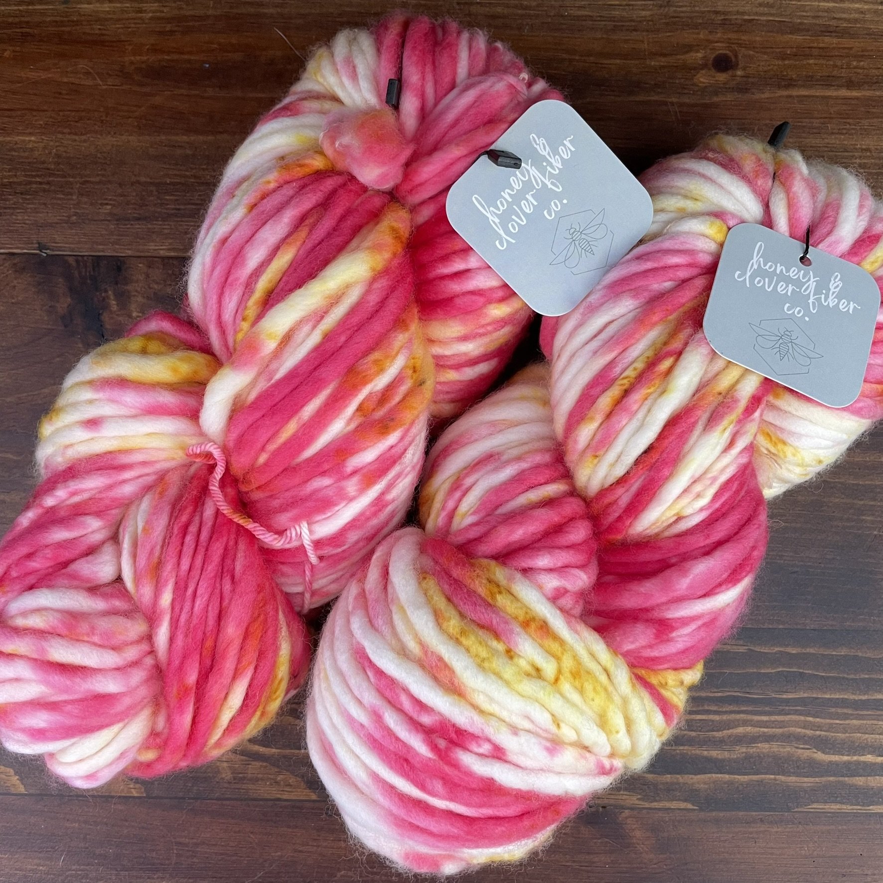 Honey & Clover Super Bulky Tequila Sunrise yarn with warm pink, yellow, and white tones.