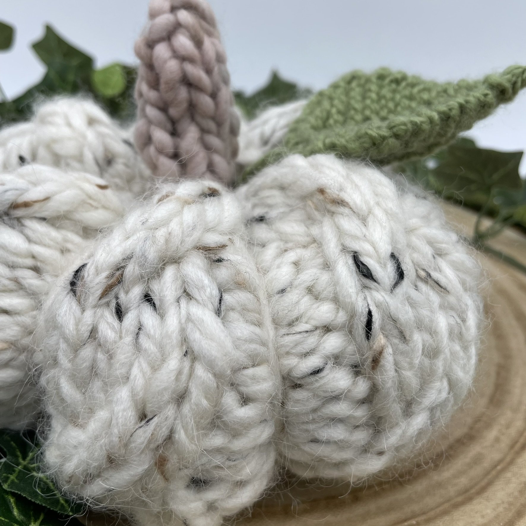Top view of a hand-knit white cable pumpkin with a green leaf and beige stem.