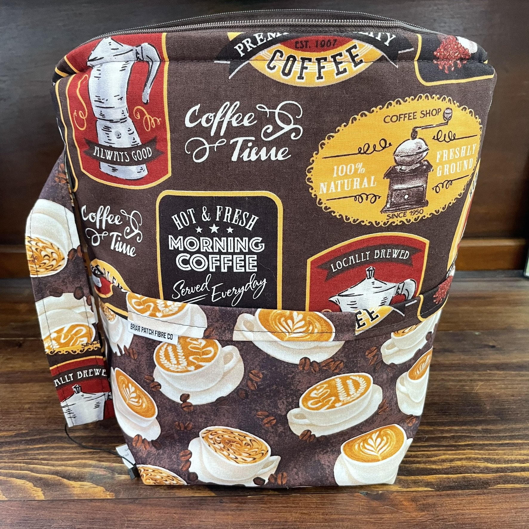 Front view of a large coffee-themed project bag, featuring vintage coffee shop designs with a brown background and multiple compartments.