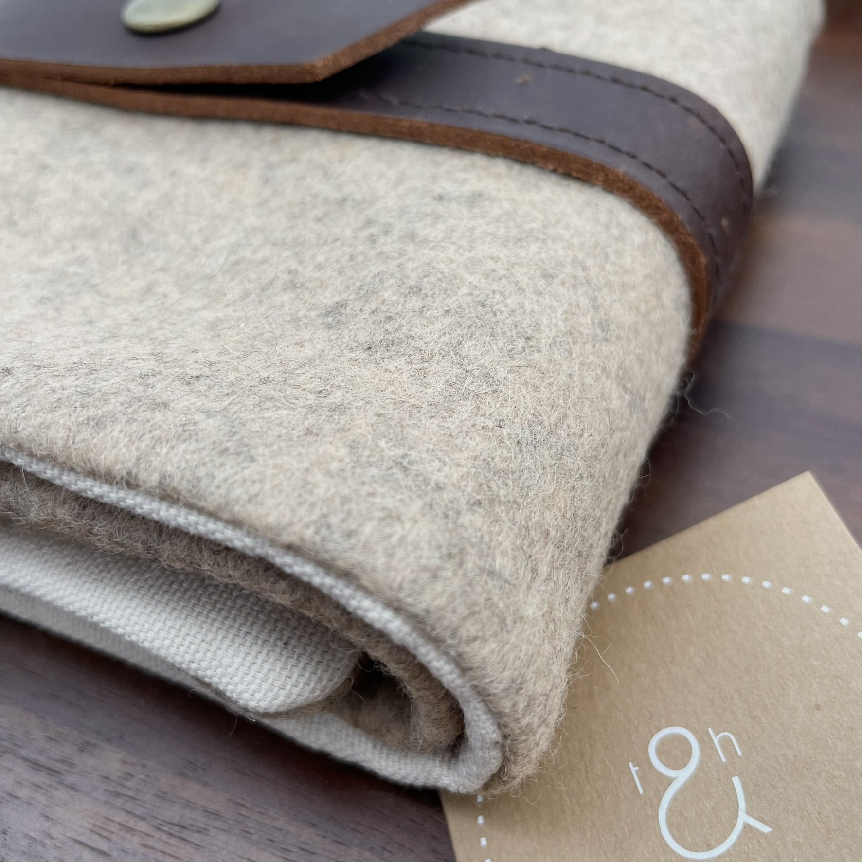 Close-up corner view of a natural wool Twig & Horn knitting tool pouch with a zipper and leather closure at an angle.