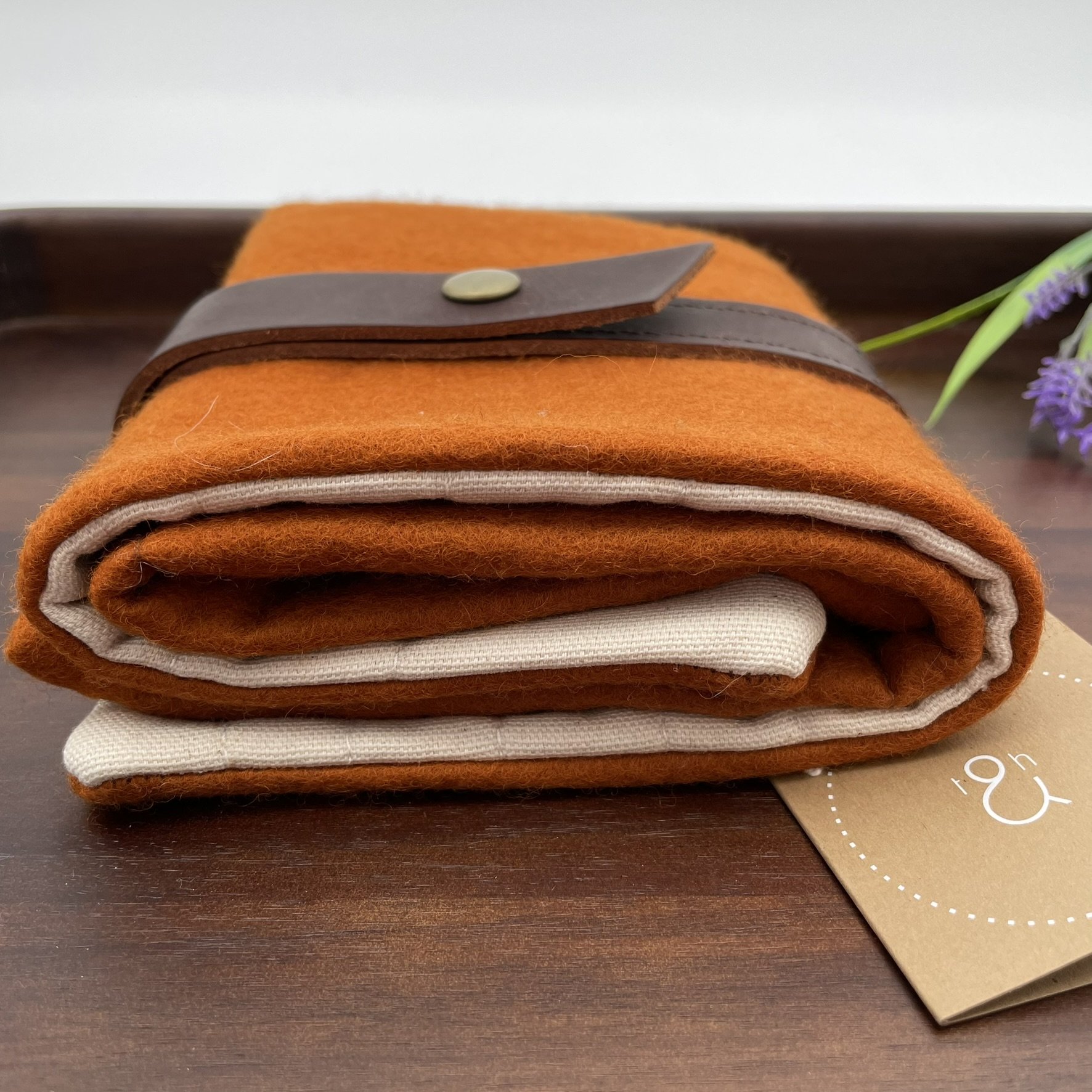 Bottom angle view of the Twig & Horn orange wool knitting tool pouch, featuring a zipper pocket and brown leather strap closure.