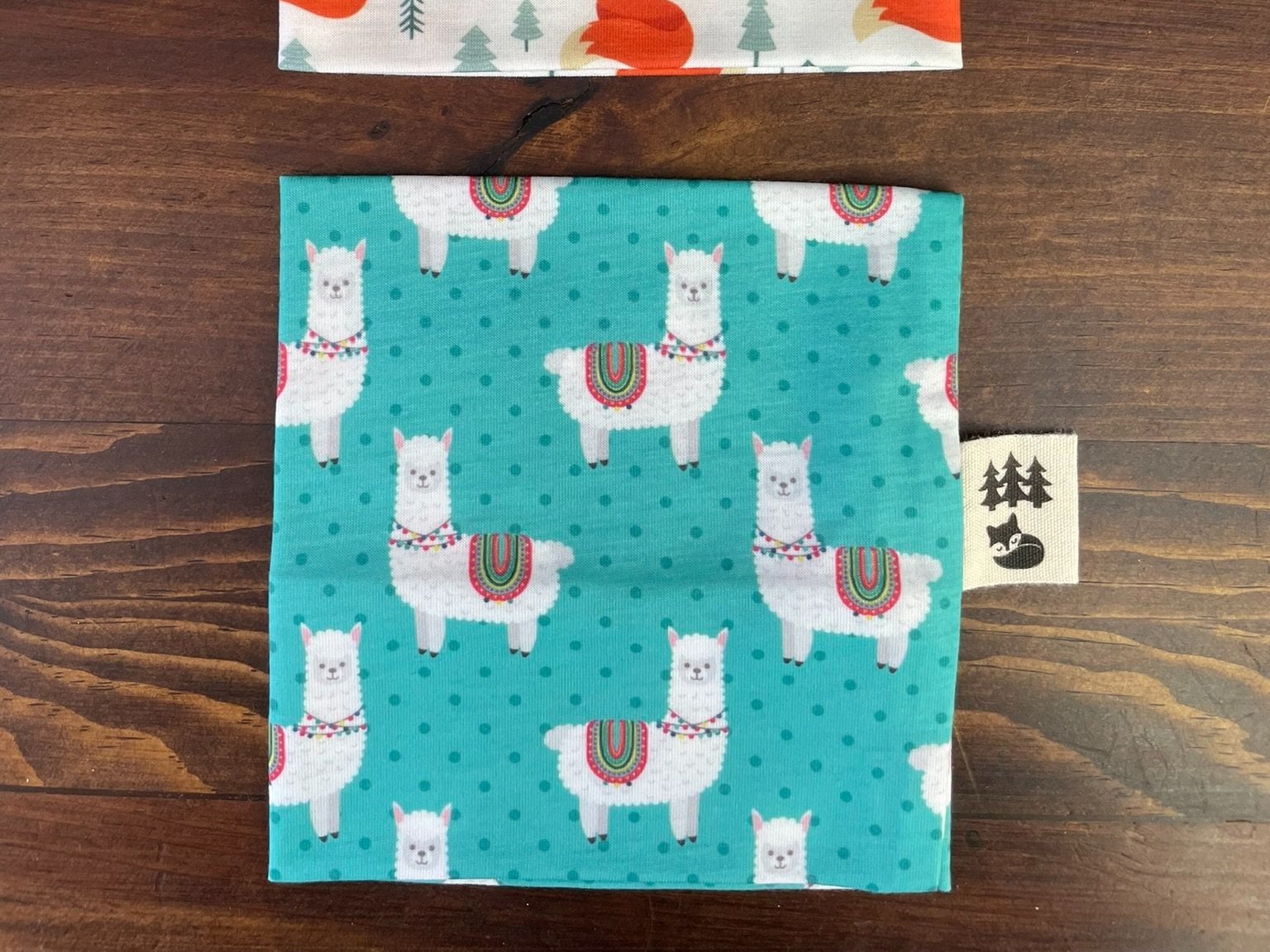 Fox & Pine yarn sweater featuring a cute llama print with colorful saddles on a teal background.