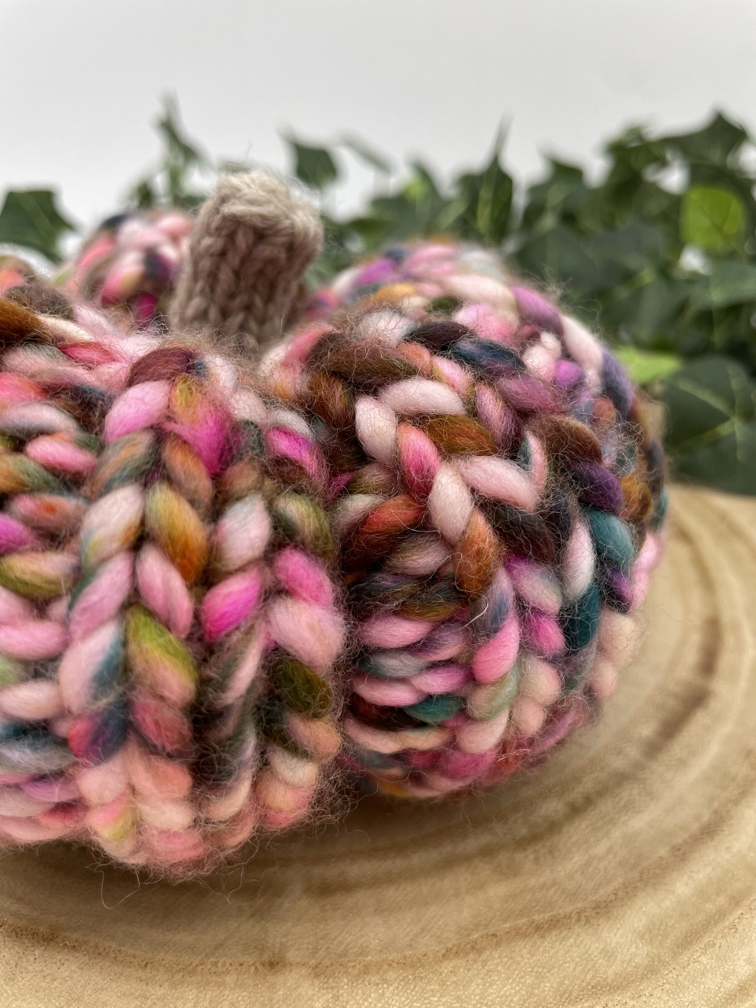 Hand-knit pumpkin in vibrant fall colors featuring multicolored yarn with shades of pink, green, orange, and beige stem.