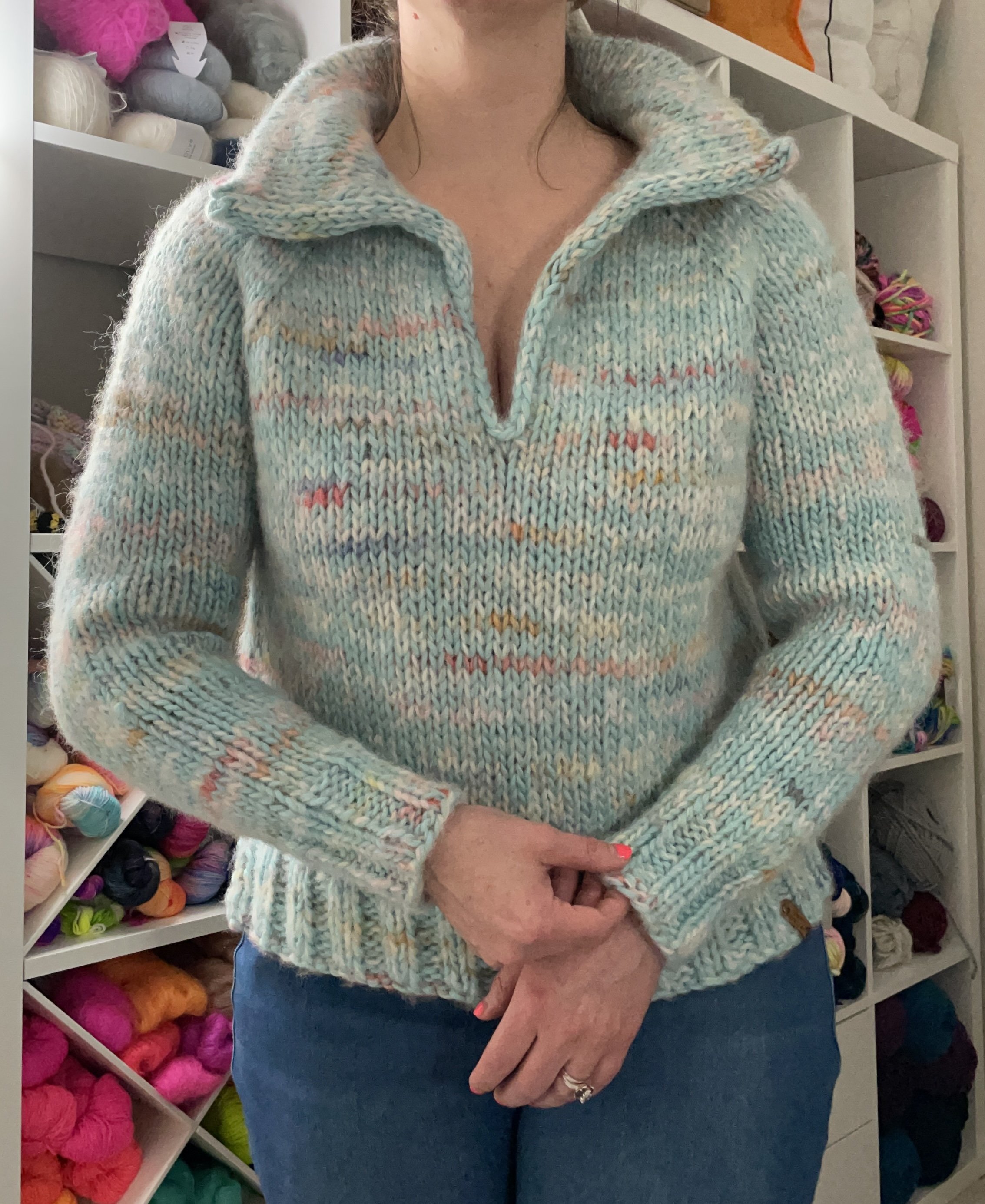 Front view of a hand-knit sky blue Wishlist pullover modeled, featuring the open collar and speckled design.