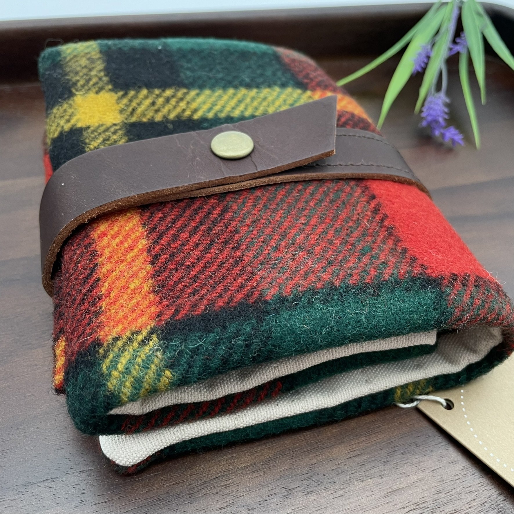 Side angle view of the Twig & Horn plaid wool knitting tool pouch with a leather strap and brass button closure.