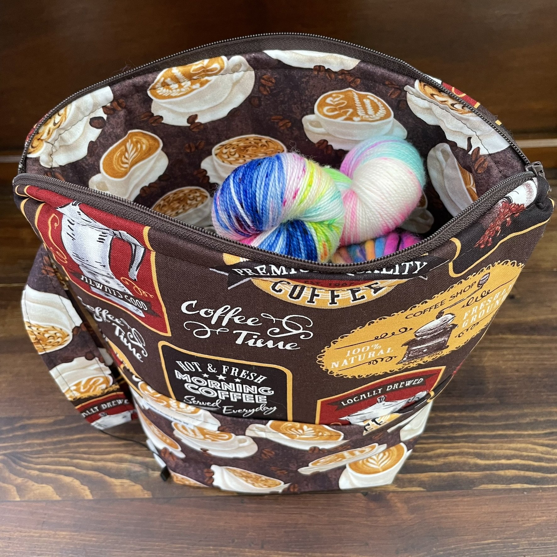 Top view of a large coffee-themed project bag filled with colorful yarn skeins, highlighting the coffee-themed fabric interior and roomy compartments.