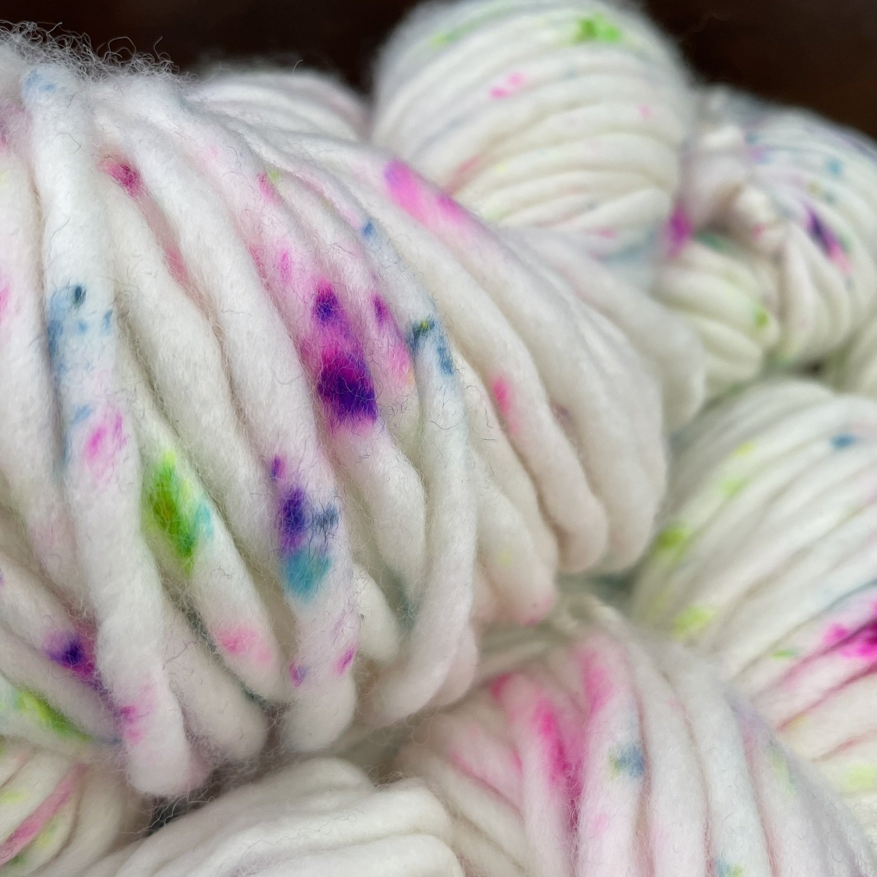 Close-up of Honey & Clover Super Bulky yarn in the Confetti colorway, featuring white yarn with bright pink, purple, green, and blue specks.