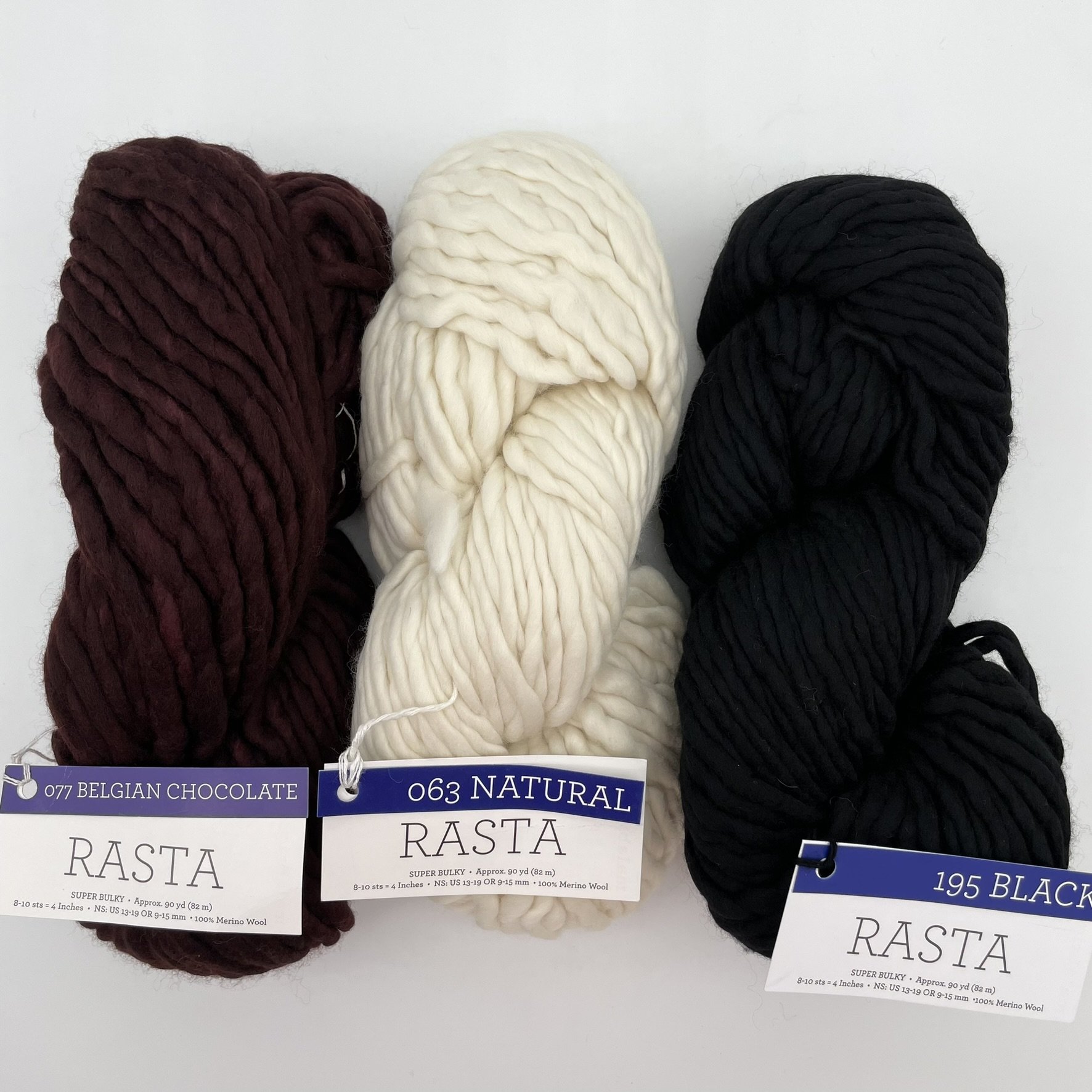 Three skeins of Malabrigo Rasta yarn in Belgian Chocolate, Natural, and Black colorways, super bulky merino wool perfect for cozy projects.