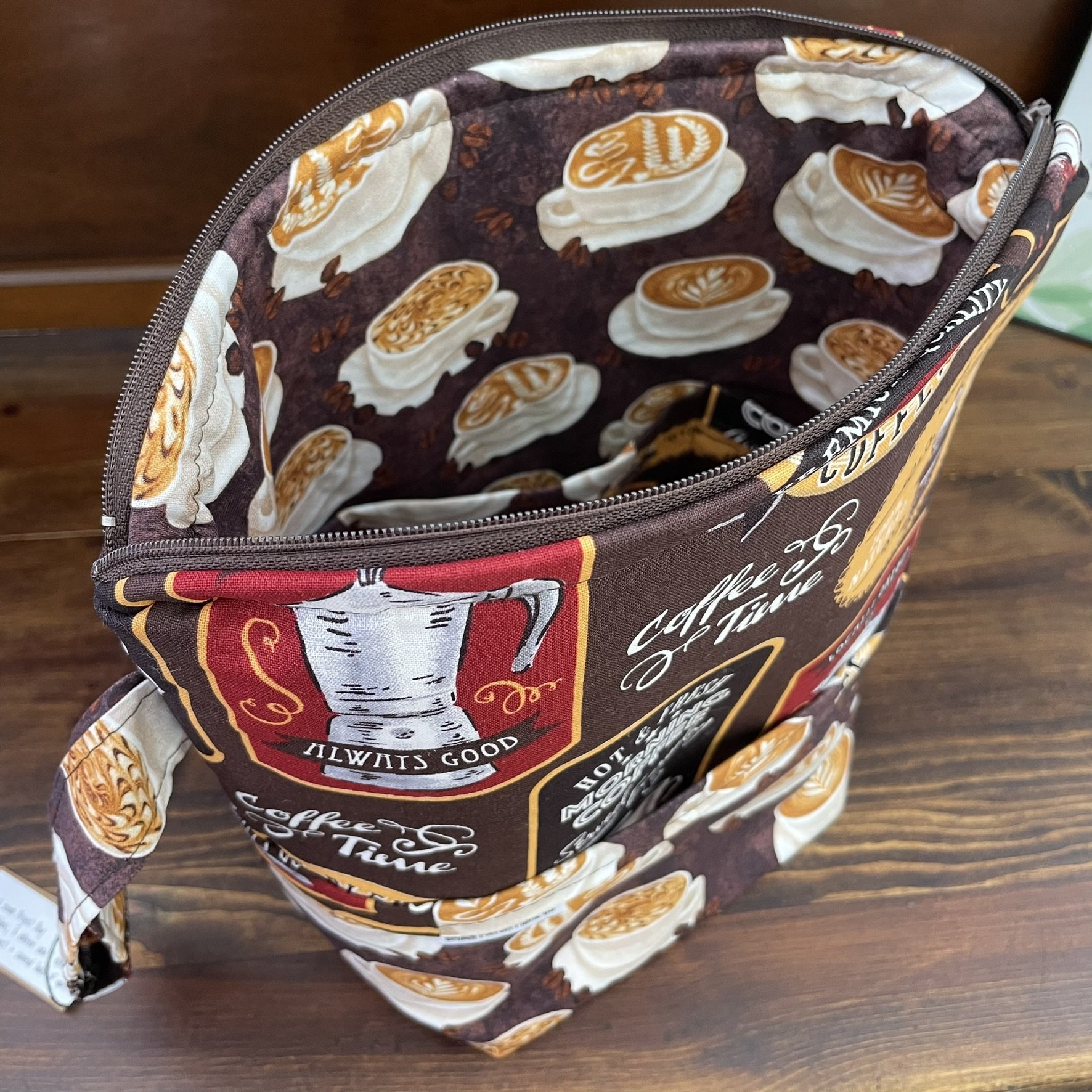 Top angled view of a large coffee-themed project bag, showcasing the spacious interior with latte cup designs and sturdy zipper closure.