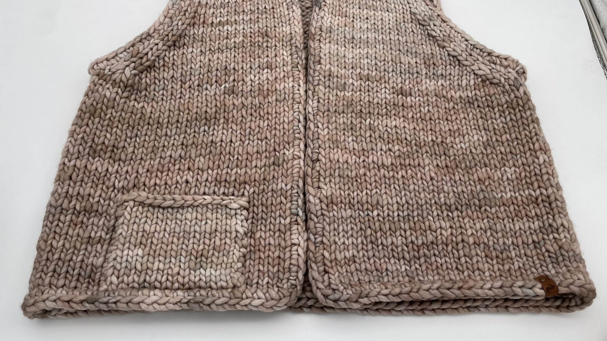 Close-up of the front pocket on a hand-knit adventurer vest in neutral tones.