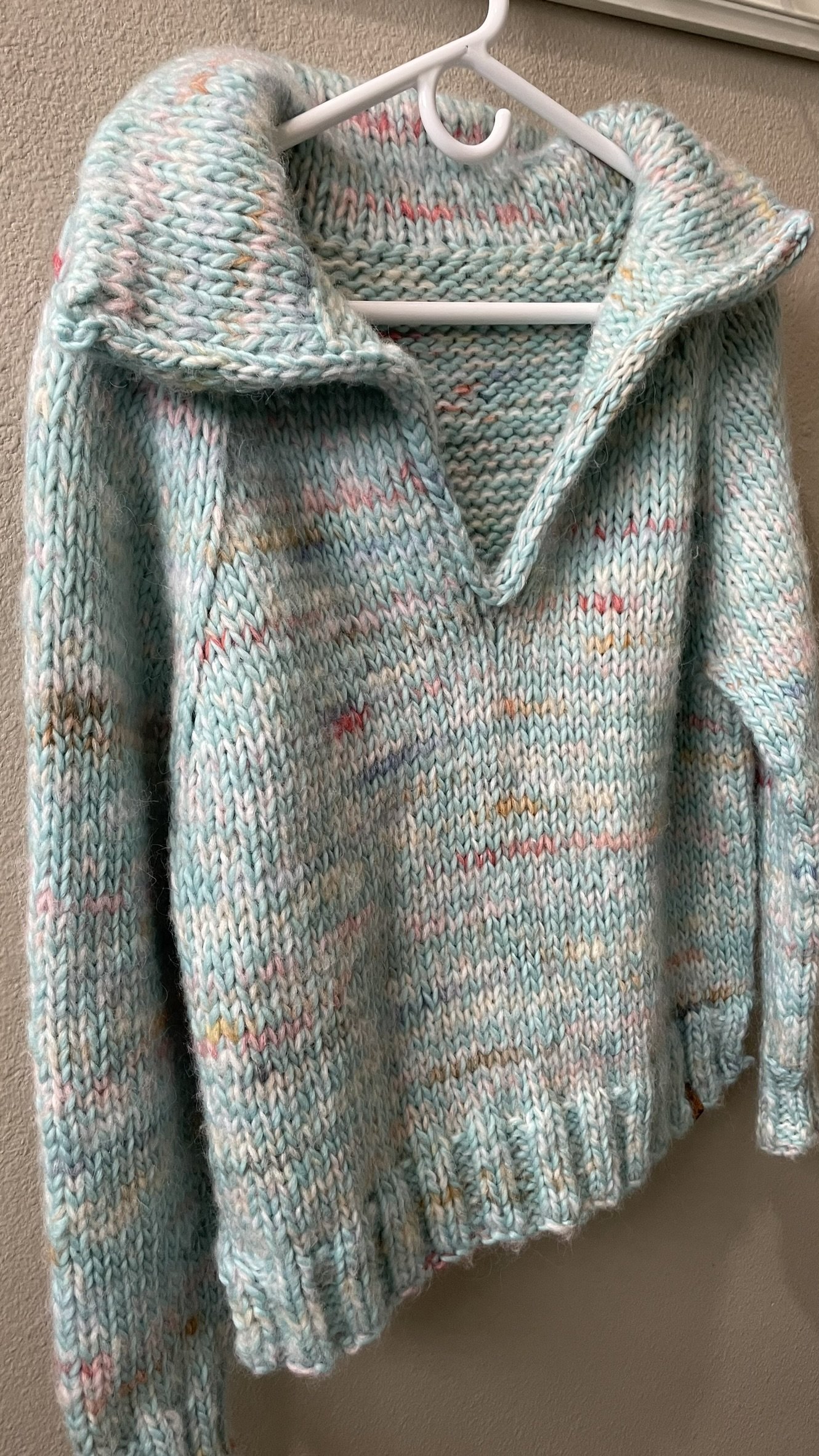 Hand-knit sky blue Wishlist pullover with an open collar, displayed on a hanger.
