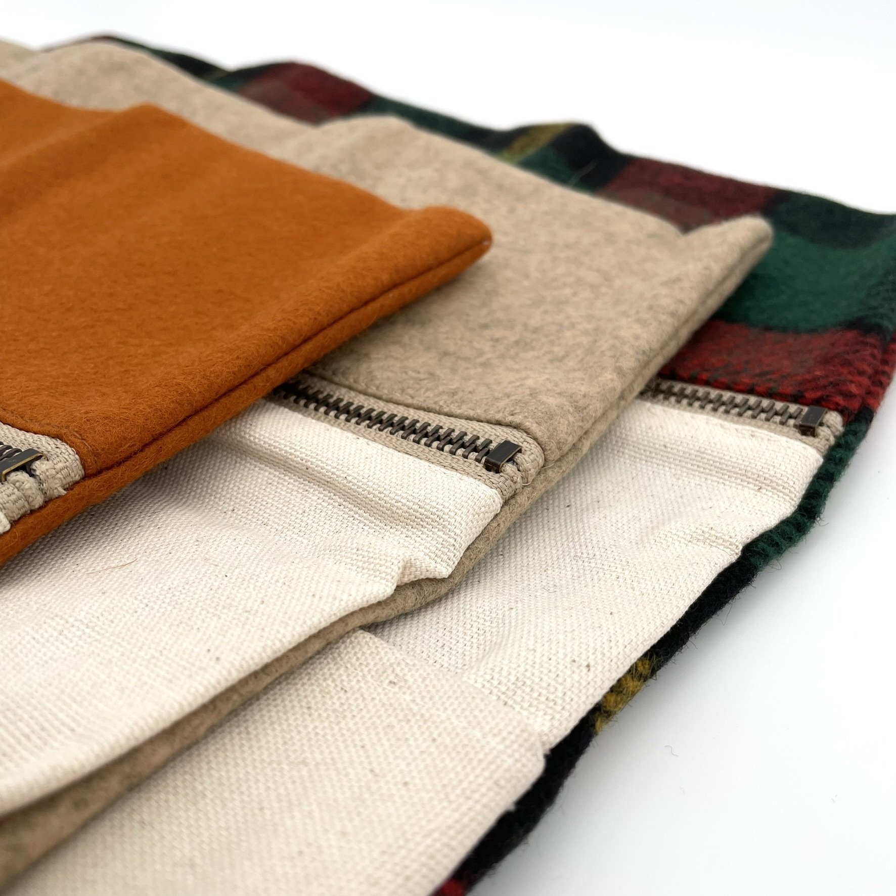 Stacked view of Twig & Horn wool knitting tool pouches in orange, natural, and plaid designs, showing leather strap closures.