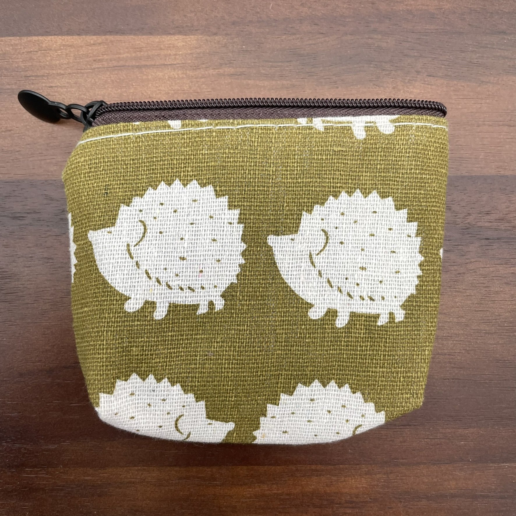 Small fabric pouch with a white hedgehog print on a green background, featuring a zipper closure.