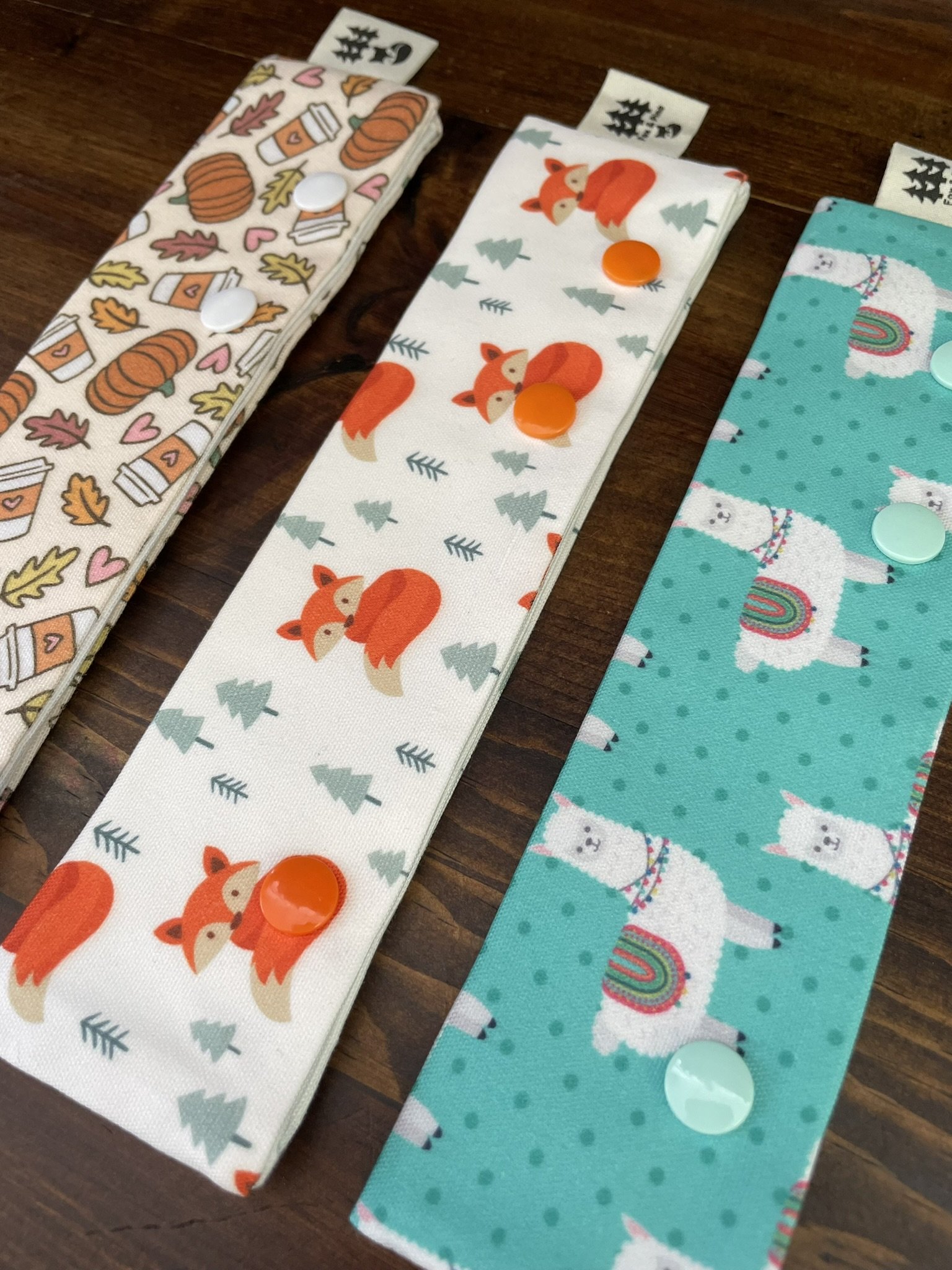 Fox & Pine double-pointed needle holders in llama, fox, and fall-themed designs, laid at an angle on a wooden surface.