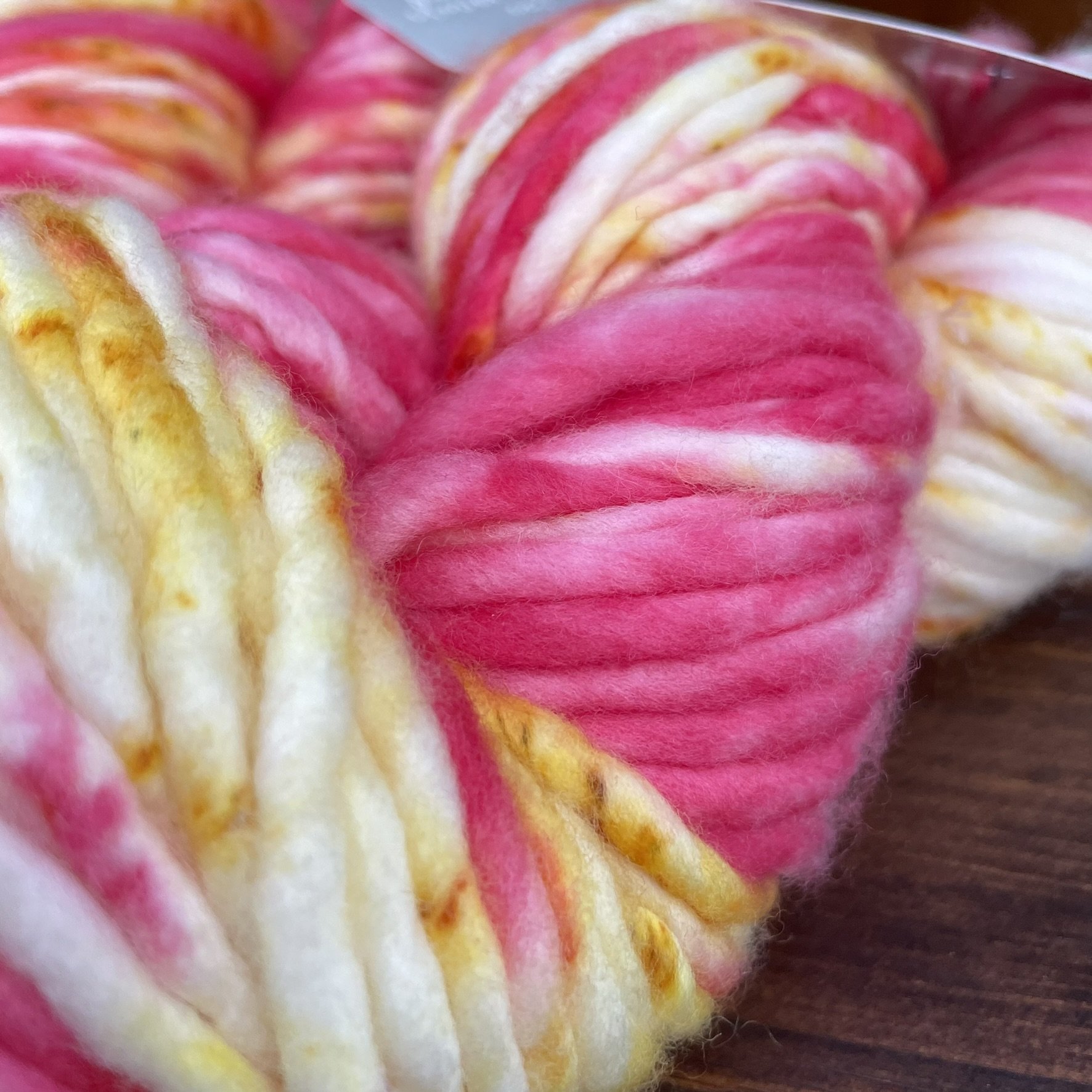 Close-up of Honey & Clover Super Bulky Tequila Sunrise yarn showing bright pink, yellow, and white wool blend.