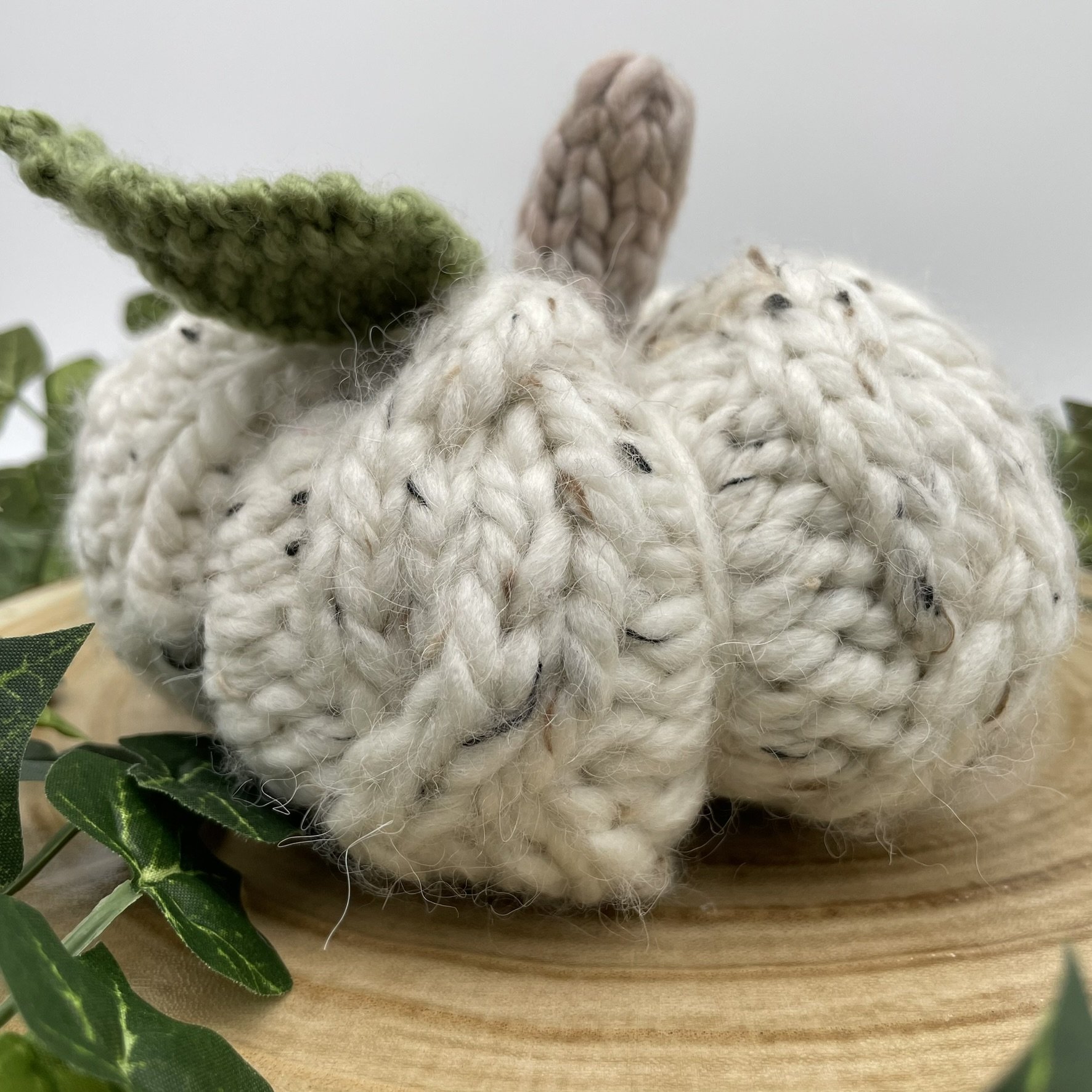 Close-up view of a hand-knit white cable pumpkin with a green leaf and textured stitches.