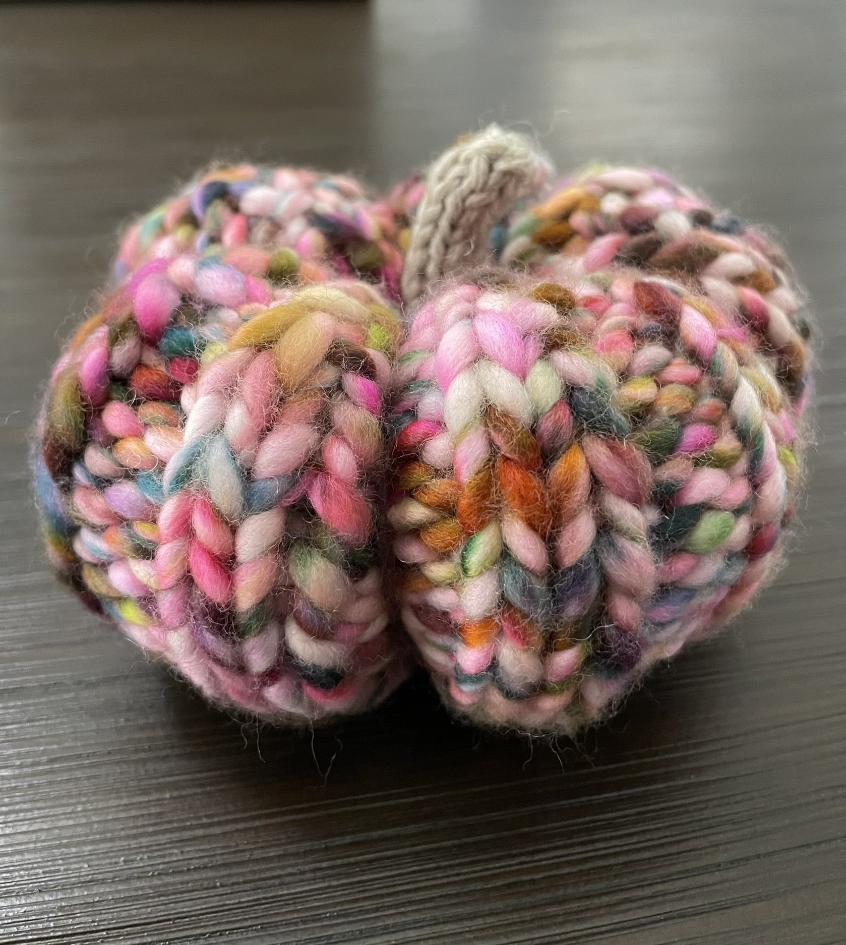 Front view of a hand-knit pumpkin in fall colors, featuring a blend of vibrant yarn and beige stem.