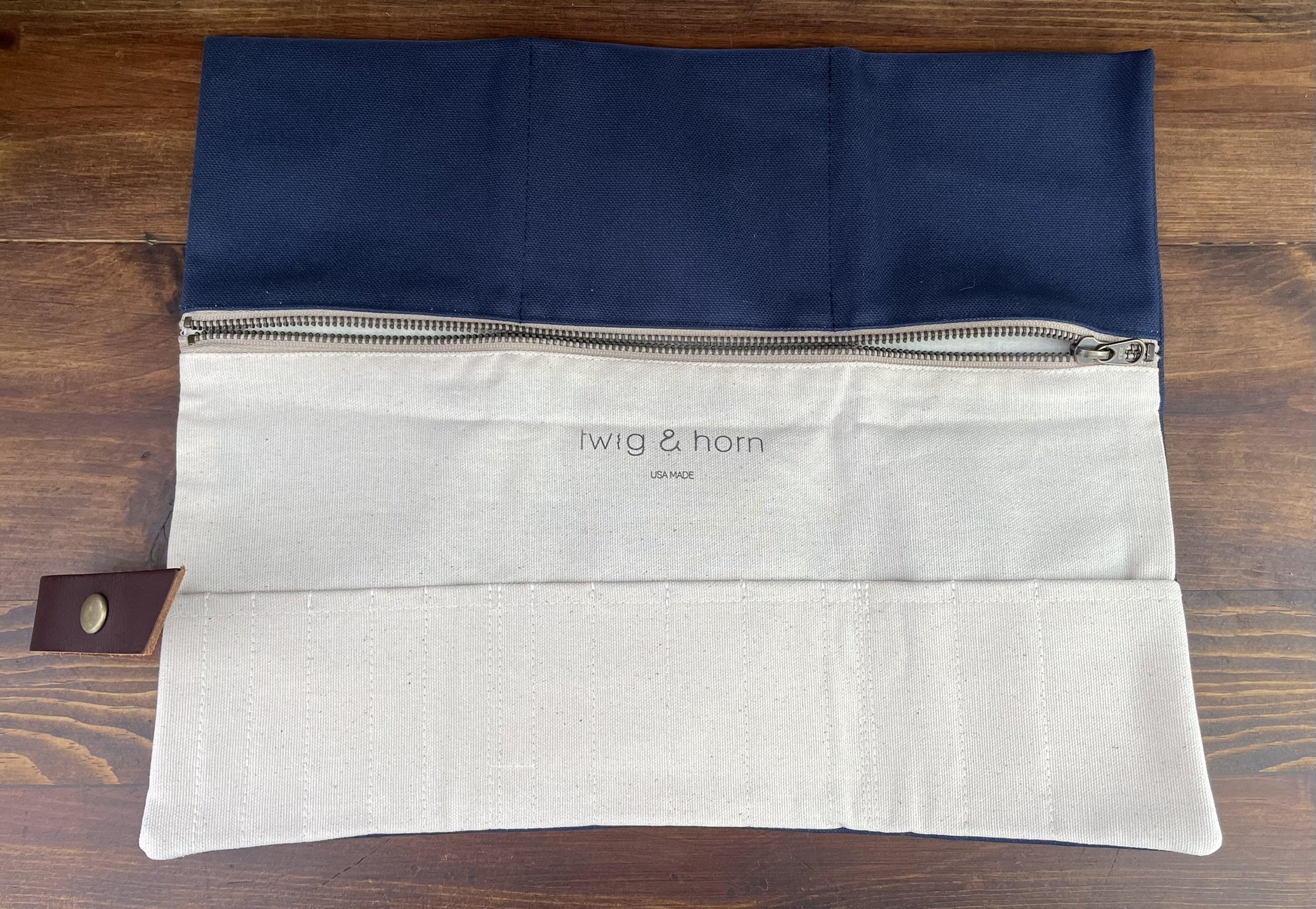 Twig & Horn interchangeable needle case in blue canvas, opened to show storage pockets and a zippered compartment with a leather strap and brass button closure.