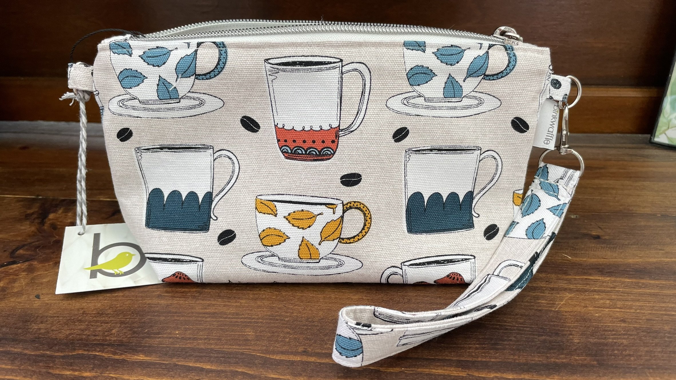 Zippered accessories pouch featuring a colorful coffee mug design, made from durable fabric with a wrist strap and secure zipper closure.