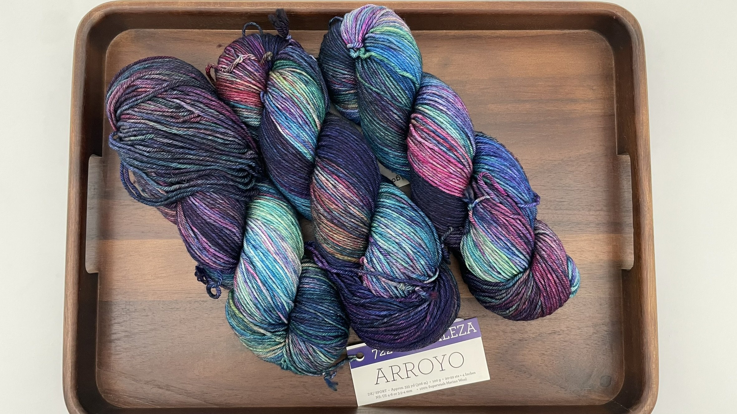 Top view of multiple skeins of Malabrigo Arroyo Fortaleza color yarn in DK/Sport weight, displayed on a wooden tray.
