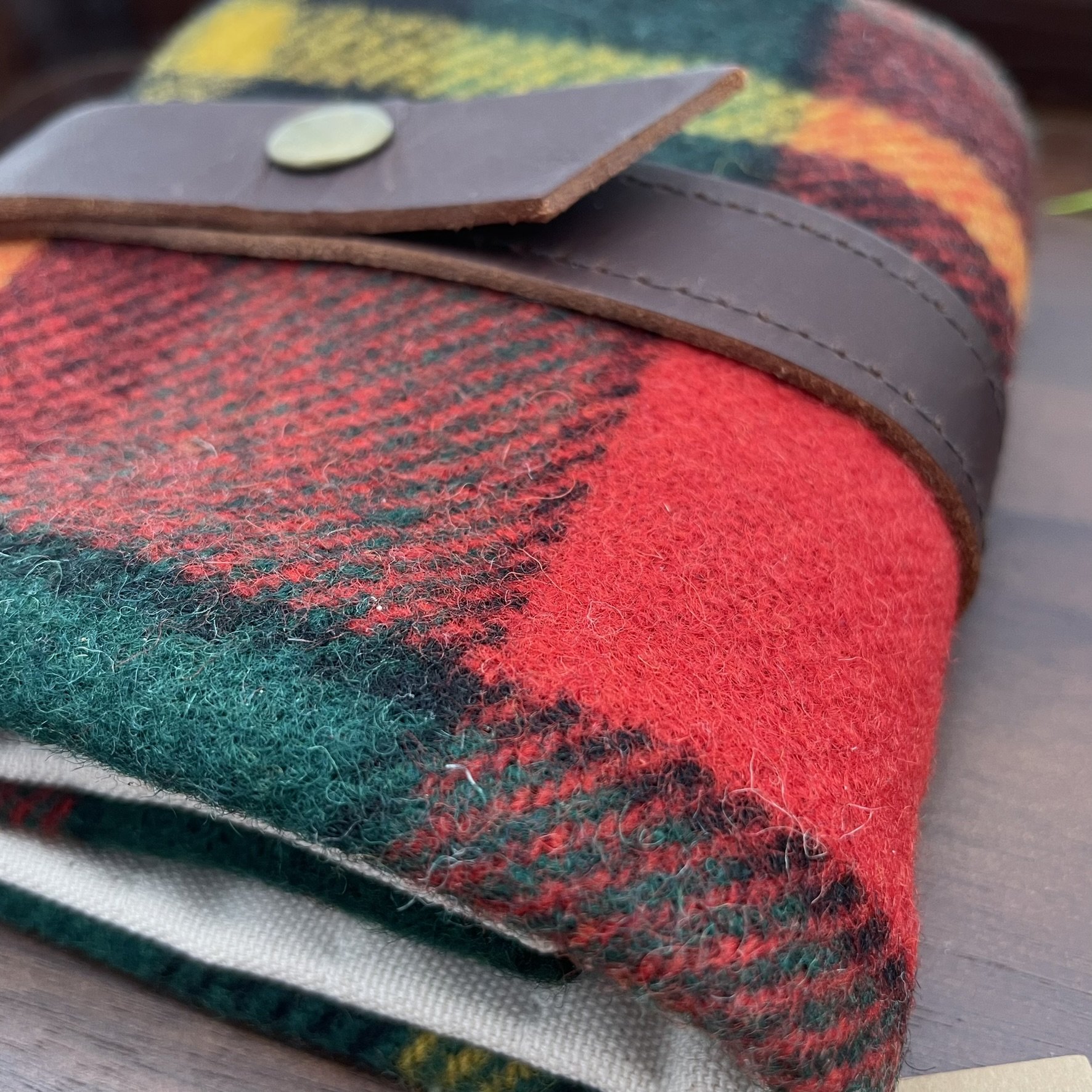 Corner angle view of a plaid wool Twig & Horn knitting tool pouch, featuring a brown leather strap and brass button.