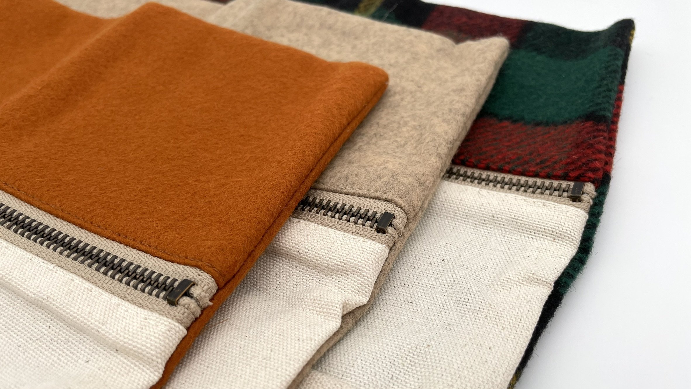 Three stacked Twig & Horn wool knitting tool pouches in plaid, natural, and orange, showing zipped compartments and interior pockets.
