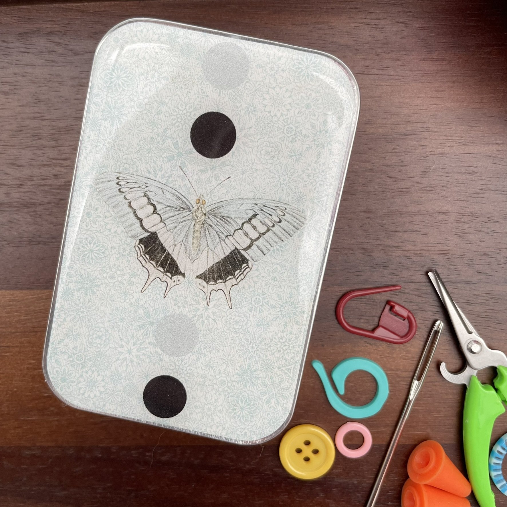 Top view of notions tin featuring detailed blue moth illustration.