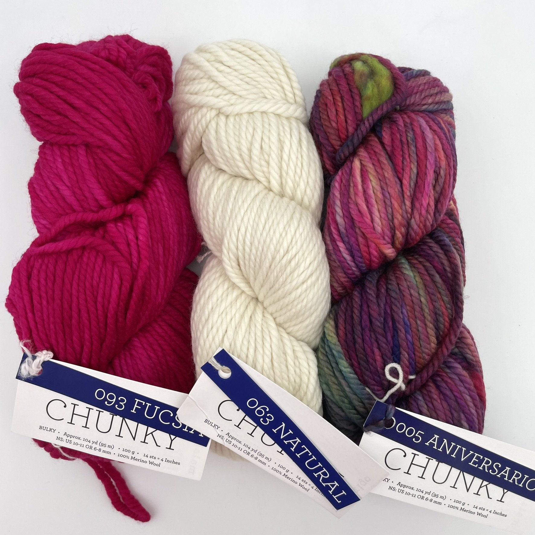 Three skeins of Malabrigo Chunky yarn in Fucsia, Natural, and Aniversario colorways. Bulky merino wool skeins for knitting or crocheting.