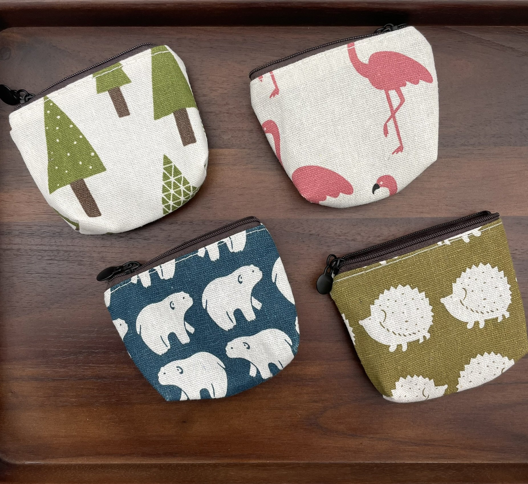 Set of four mini fabric pouches featuring designs of trees, flamingos, polar bears, and hedgehogs, all with zipper closures.