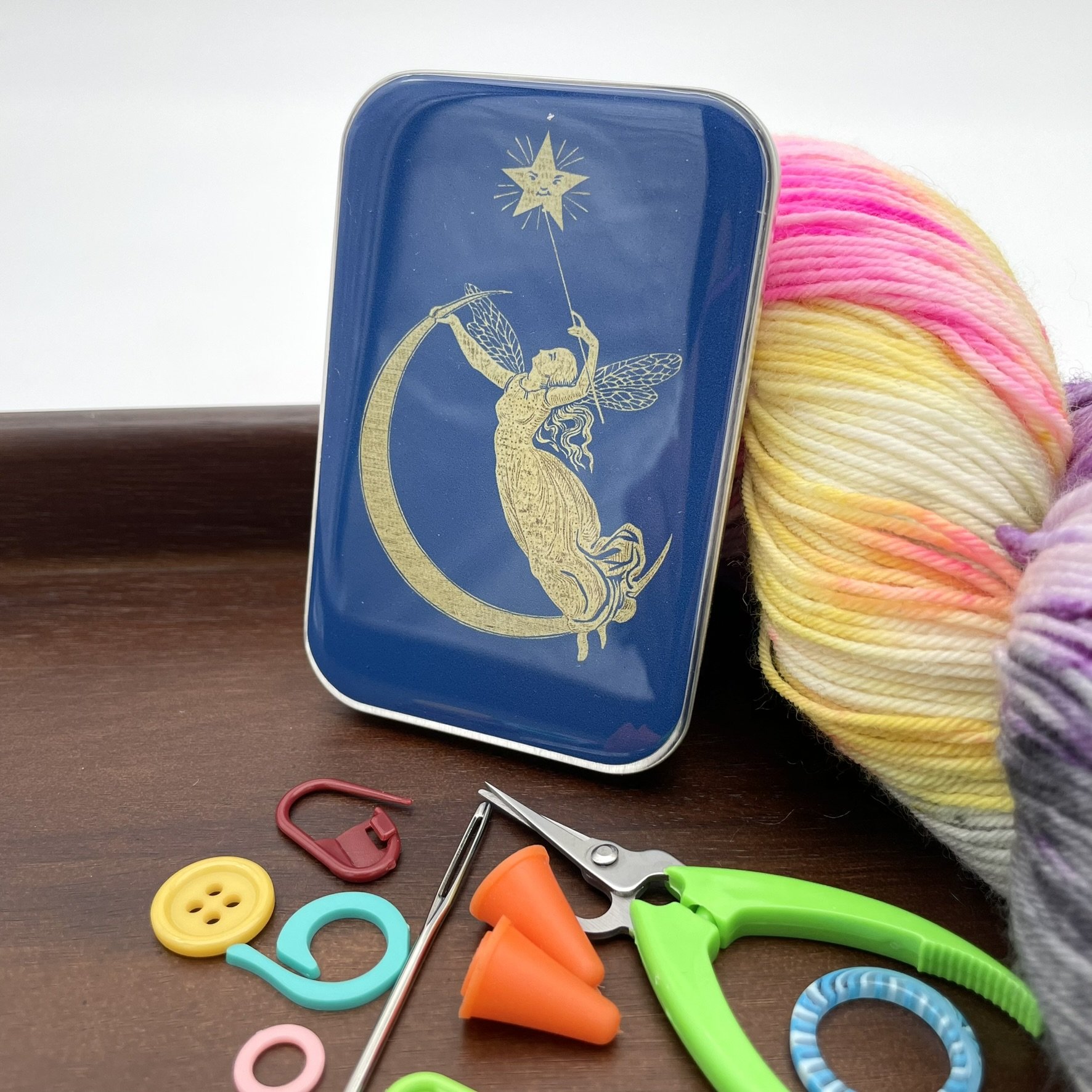 Upright view of a blue fairy design notions tin featuring a gold fairy reaching for a star with a crescent moon below.
