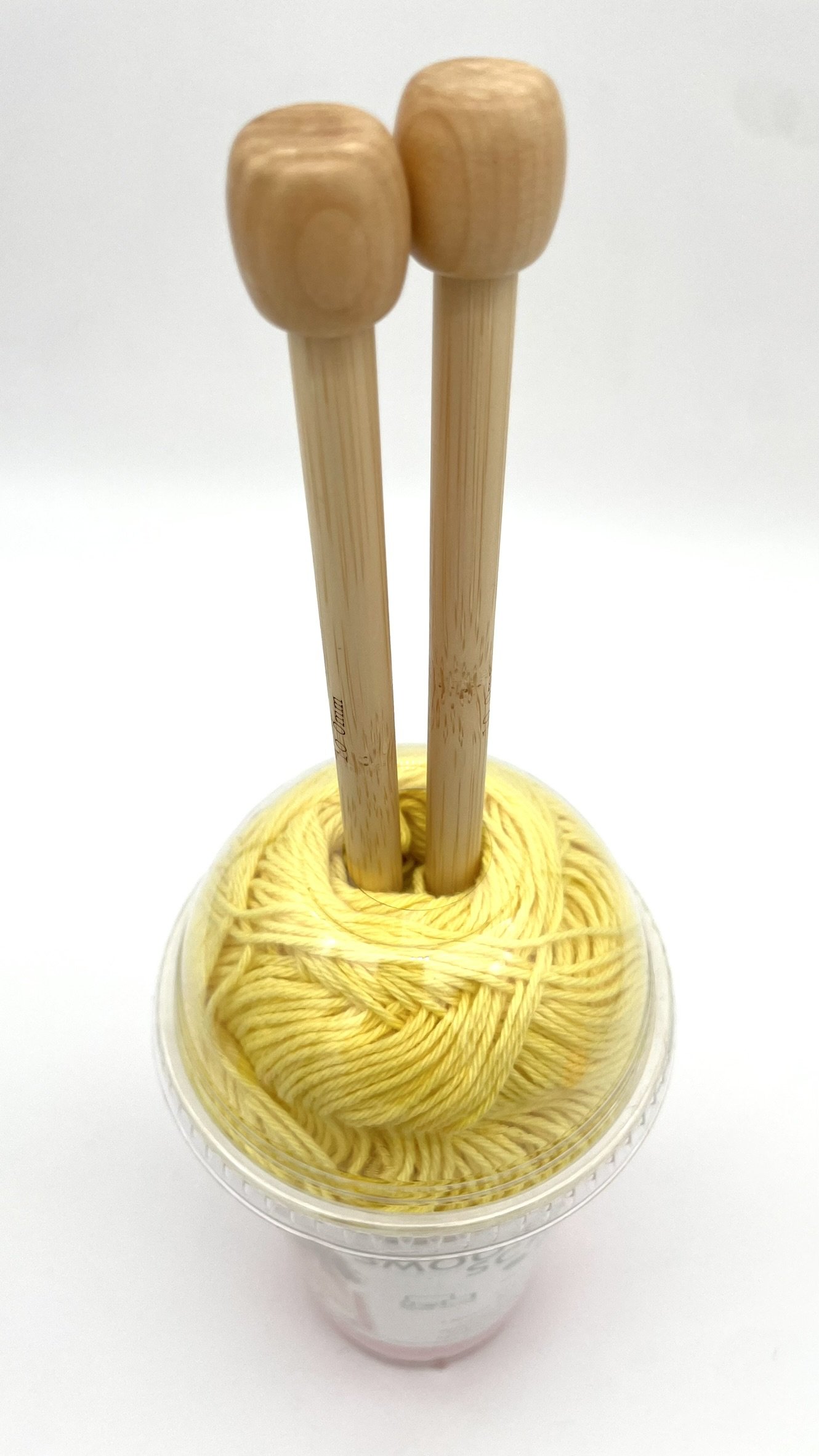Top-down view of DIY Smoothie Scarf kit in yellow and pink with bamboo knitting needles.