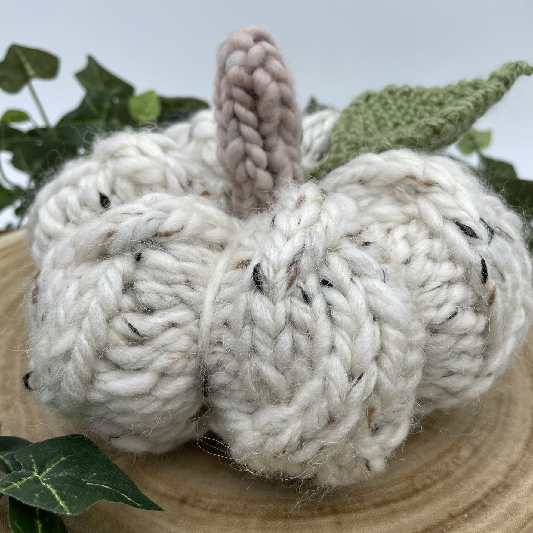 Side view of a hand-knit white cable pumpkin with a textured stitch pattern and green leaf.