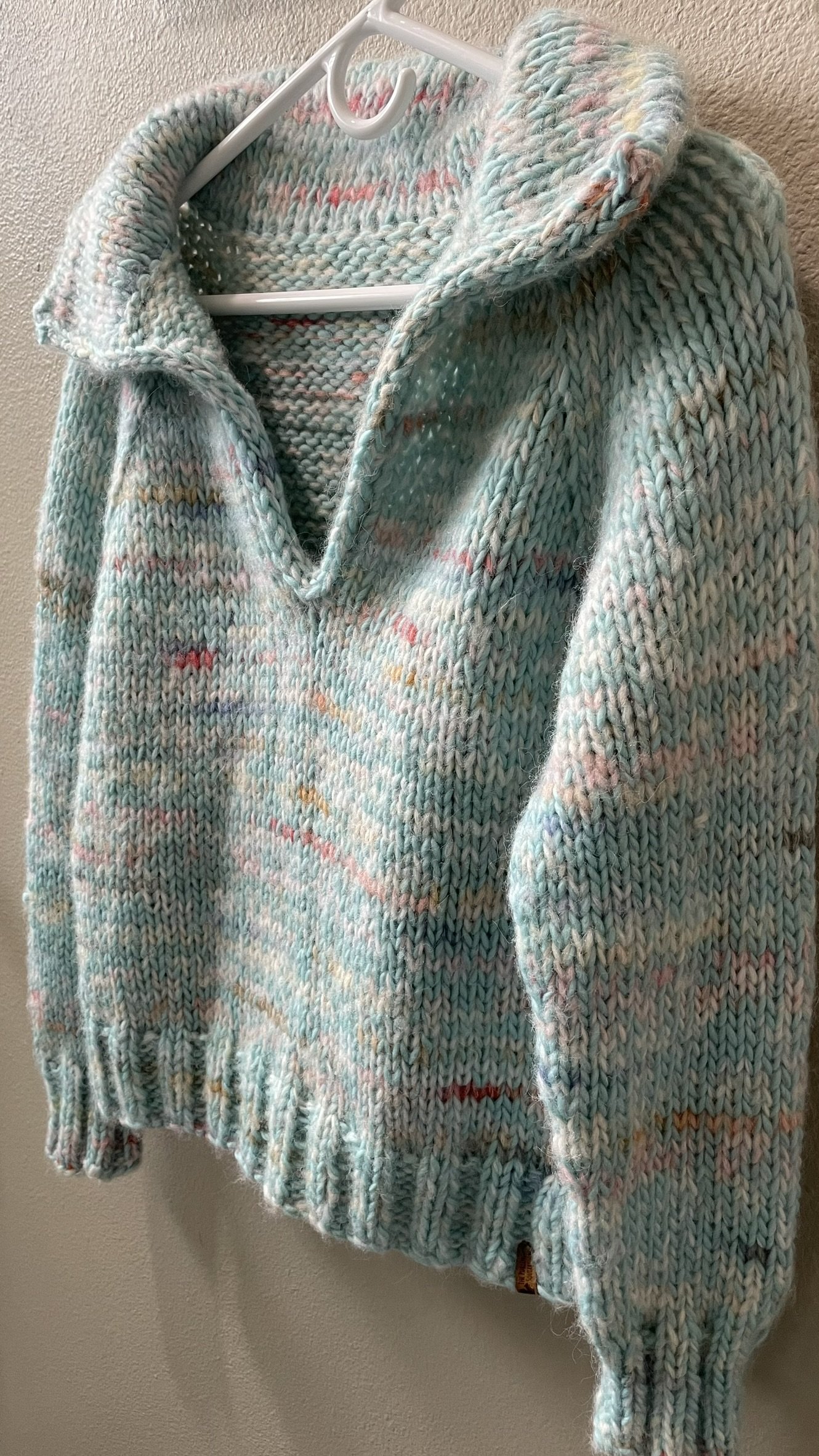 Hand-knit sky blue Wishlist pullover with colorful speckles, hanging on a hanger.