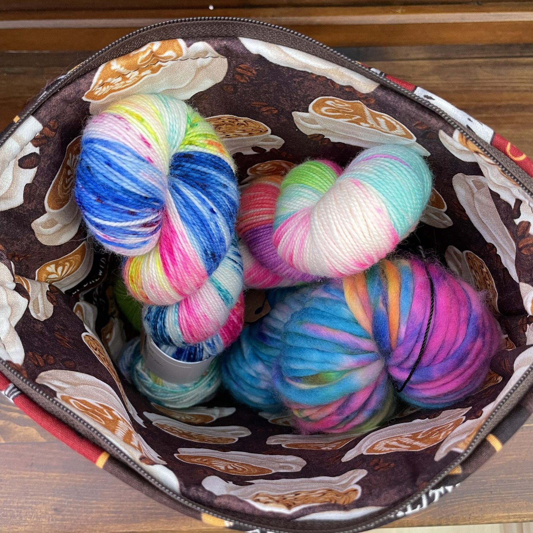 Interior view of a large coffee-themed project bag filled with colorful yarn skeins, featuring latte art fabric lining.