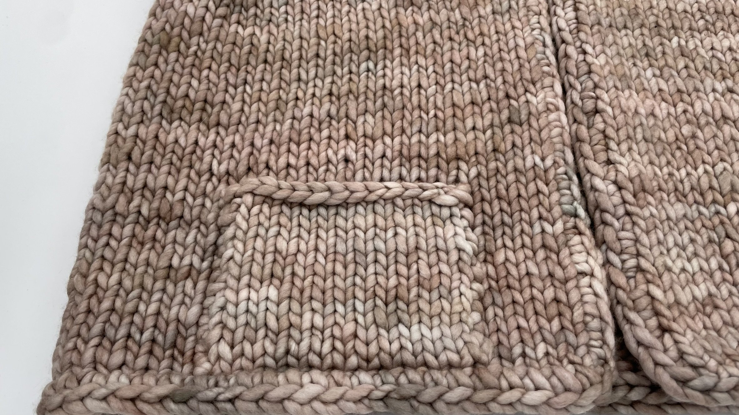 Detailed view of the front pocket on a hand-knit adventurer vest in natural wool tones.