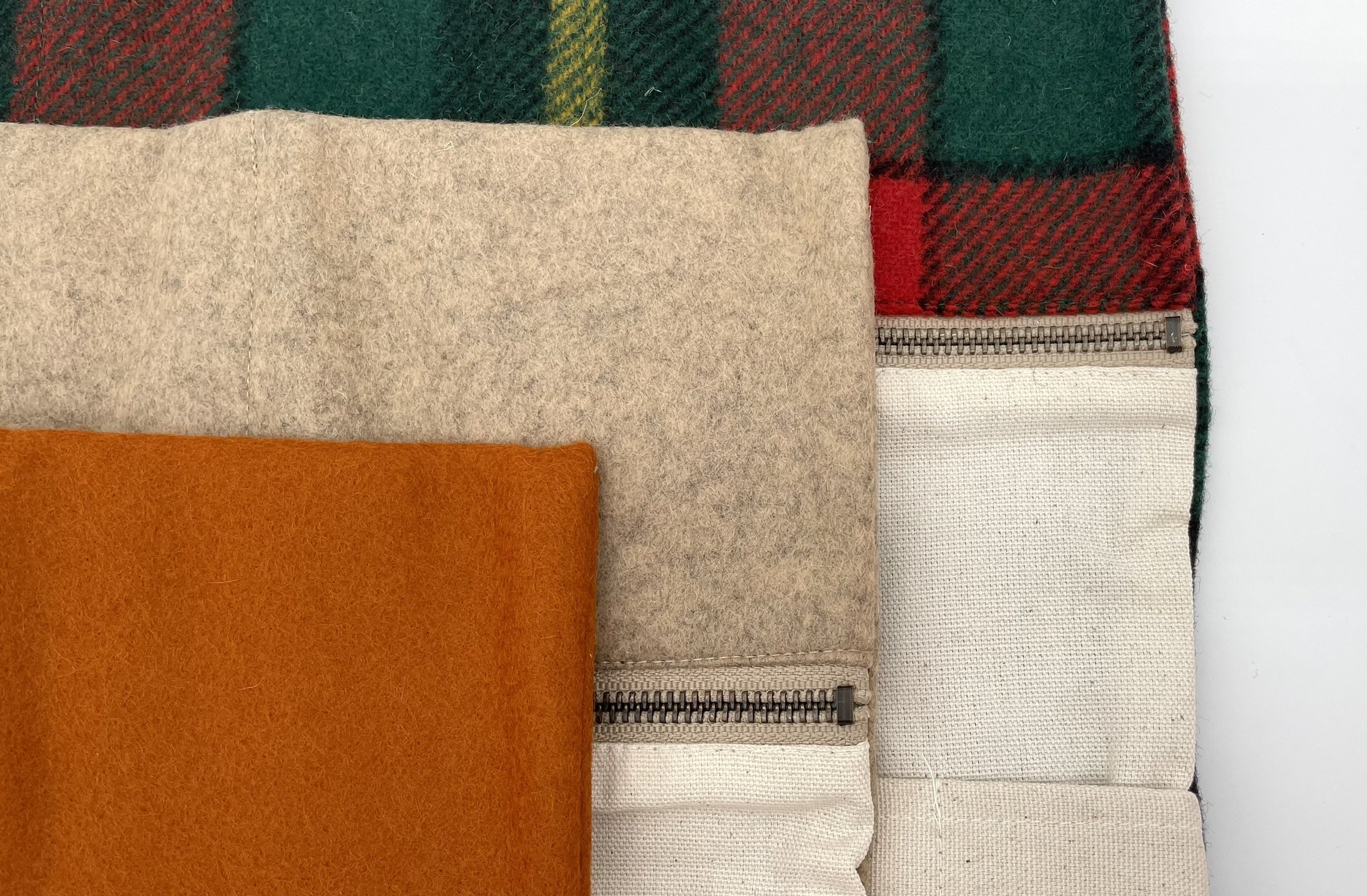 Top view of three Twig & Horn knitting tool pouches in plaid, natural, and orange wool, open to show storage compartments.