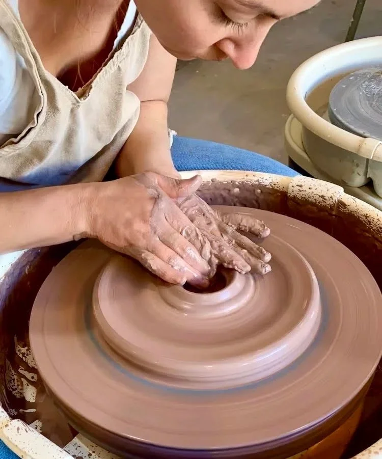 Person shaping clay on a pottery wheel in a studio.