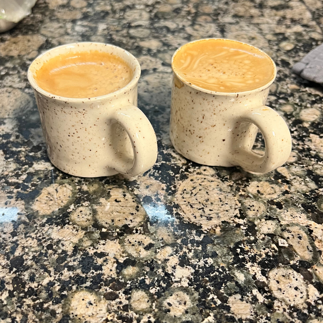 Two small ceramic mugs filled with coffee on a speckled granite countertop.