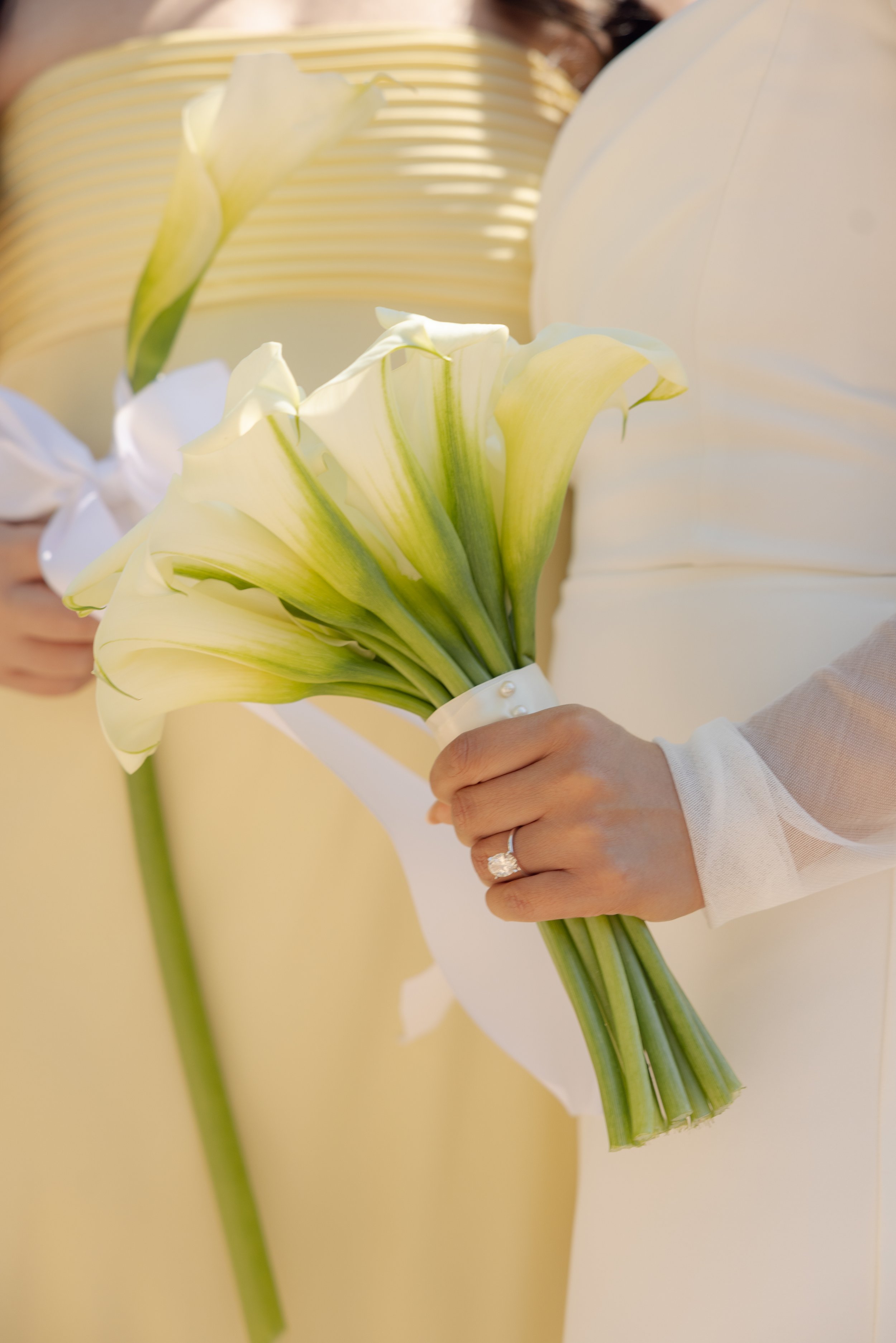 Person holding a bouquet of white and green calla lilies, with wedding ring visible on hand.
