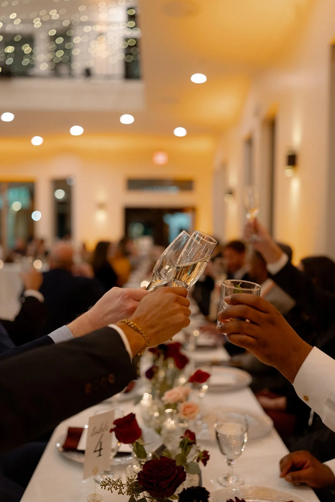 People raising glasses in a toast at a formal dinner event with elegant table decorations and warm lighting. In Dallas Fort Worth Texas