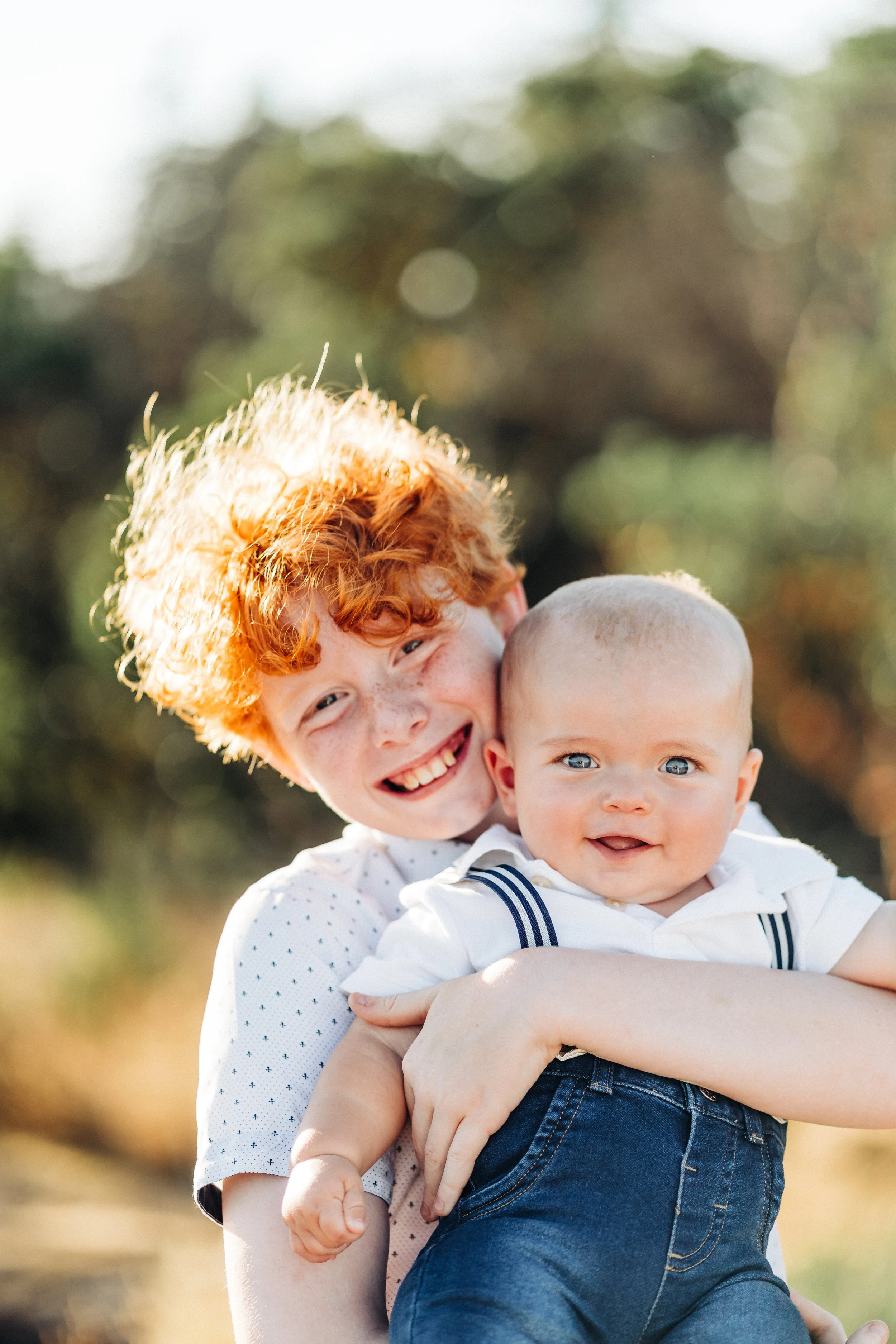 Smiling child holding a baby outdoors in a sunny setting.