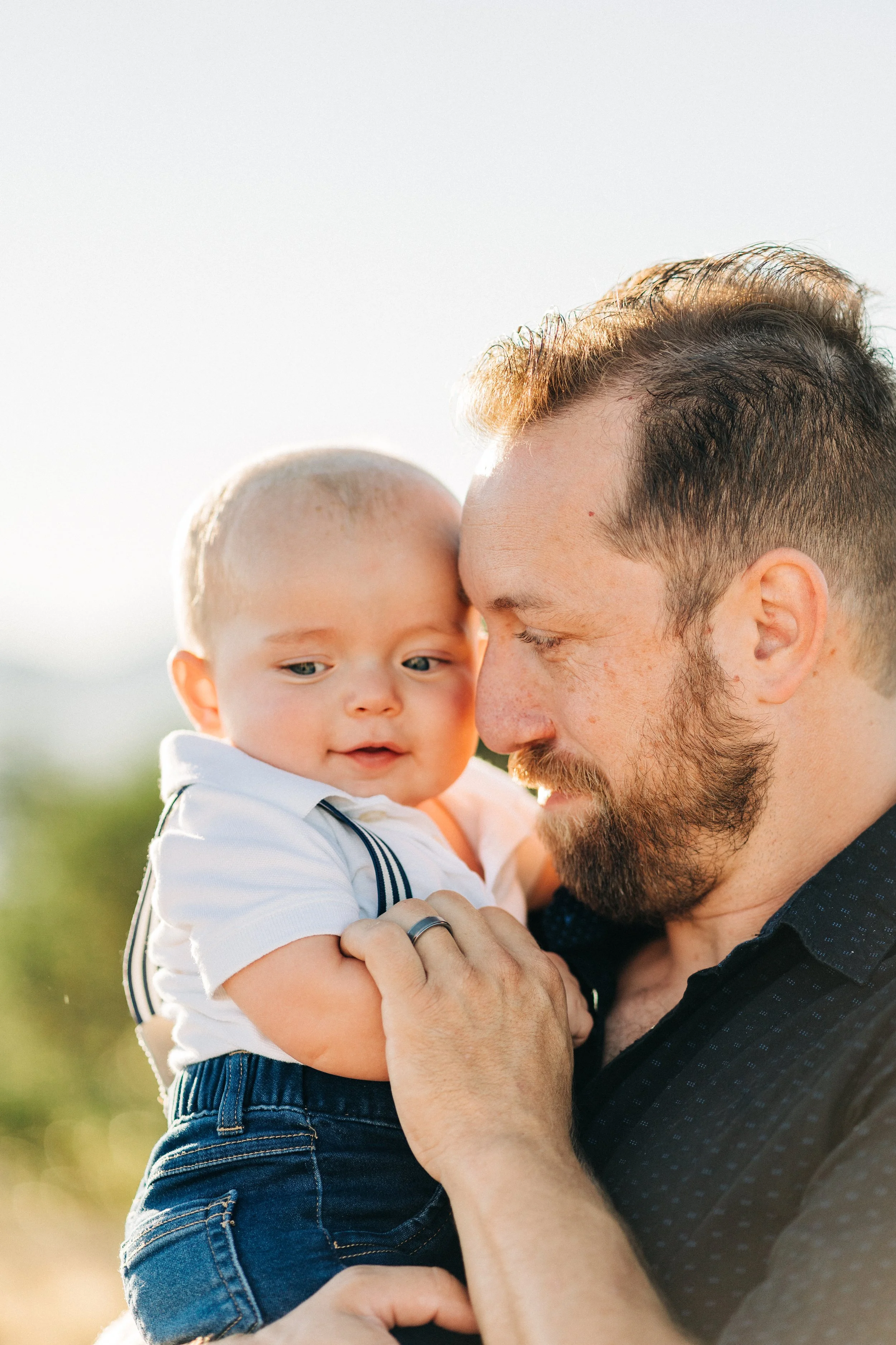 Man holding a baby closely outdoors.
