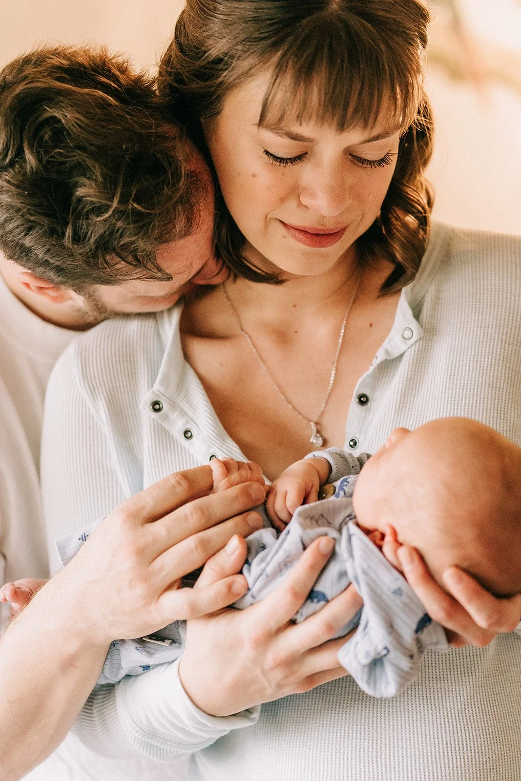 A woman holding a newborn baby in her arms while a man gently touches the baby's hand, all with joyful expressions.